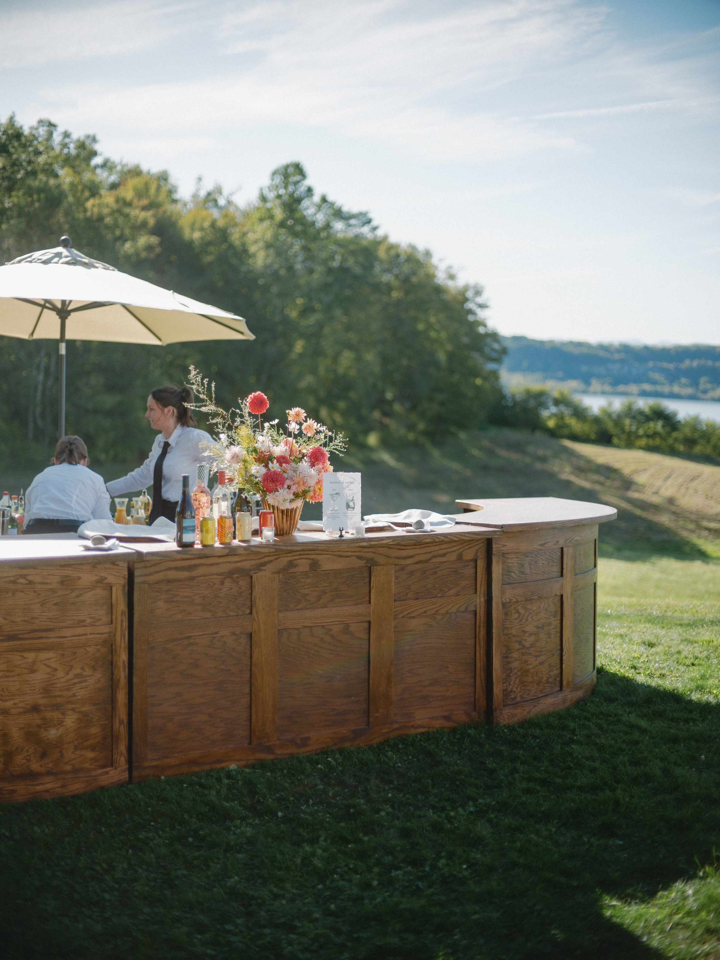 Outdoor wooden bar set on lawn with floral arrangements and scenic views