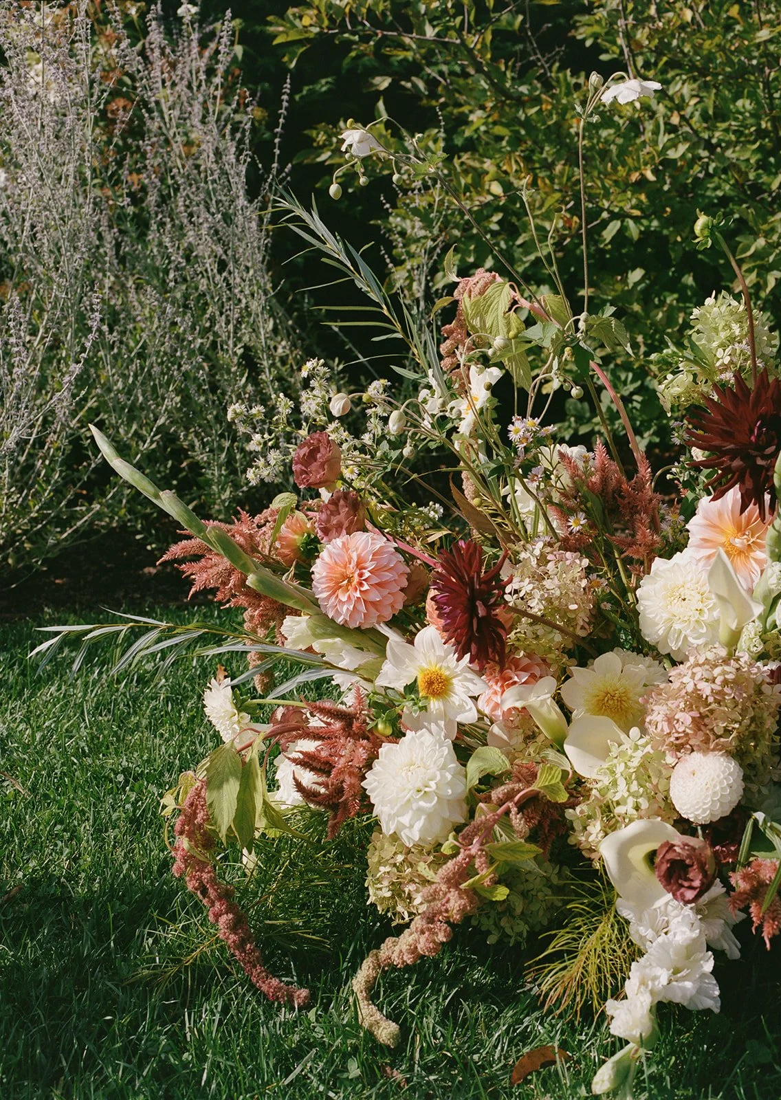 Grounded floral arrangement featuring blush dahlias, cream blooms, and wild greenery set in the grass.
