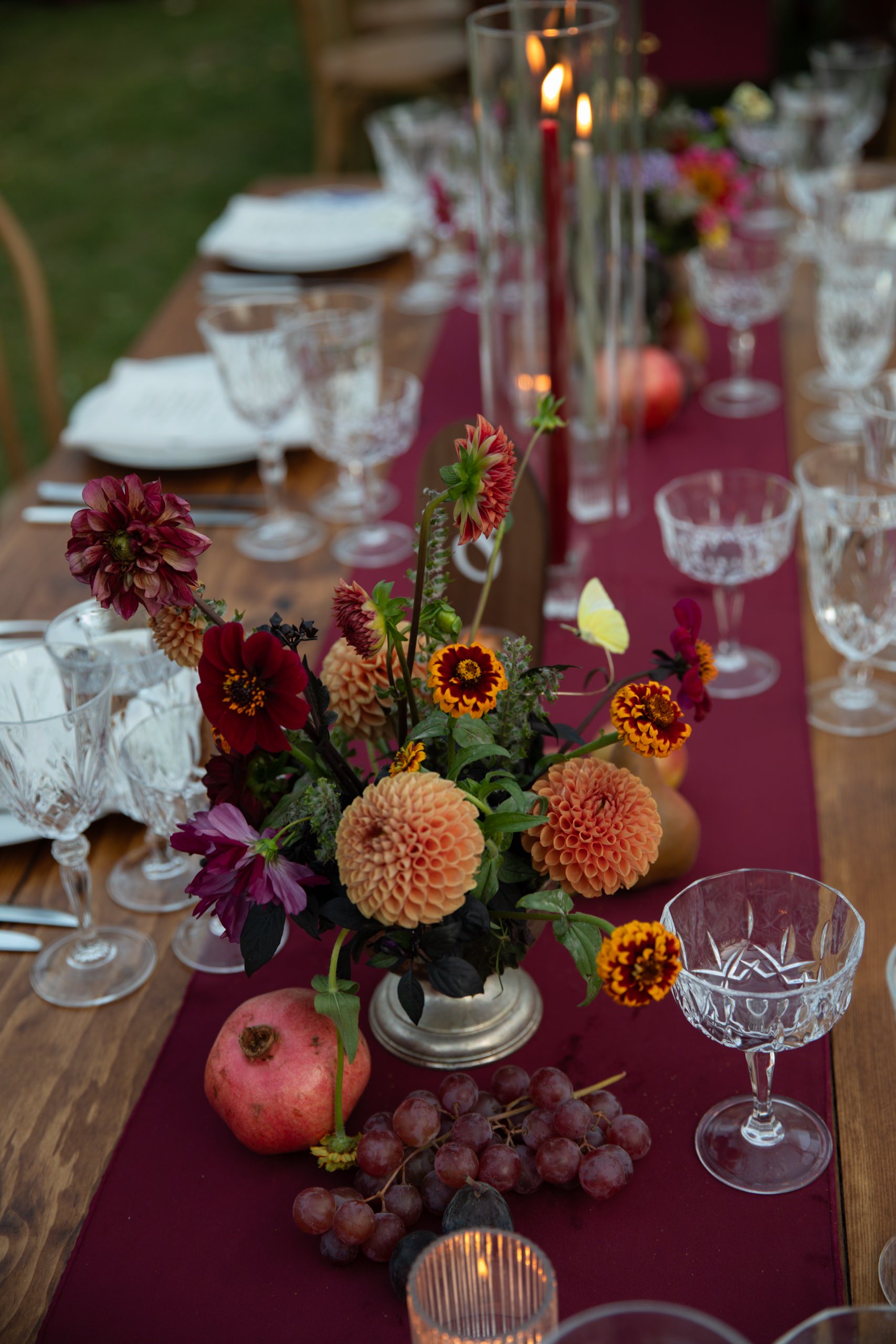 Abundant floral centerpiece with dahlias and late-season flowers styled alongside glassware and taper candles