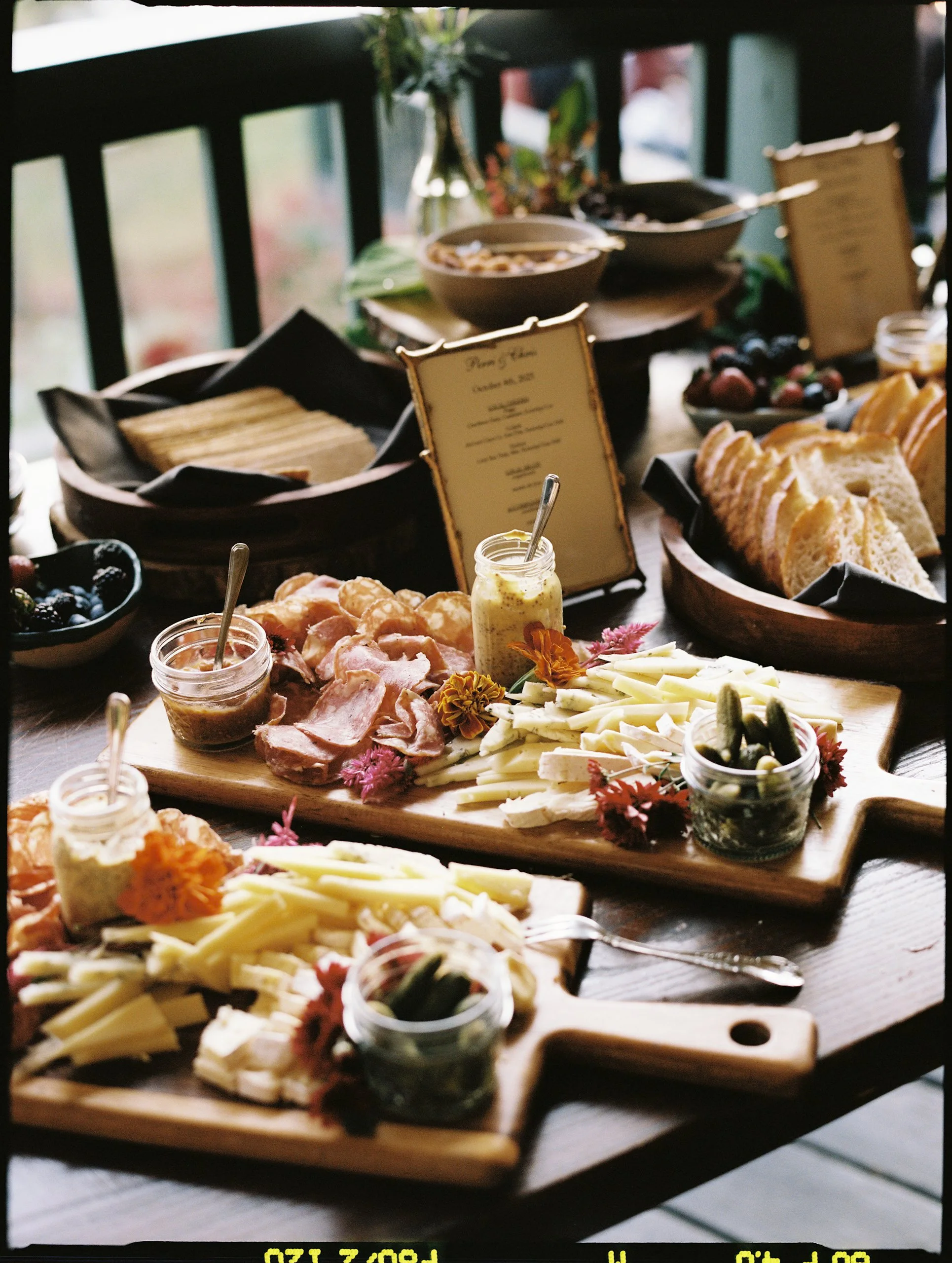Cheese and charcuterie display accented with seasonal flowers and greenery for a garden-inspired cocktail hour