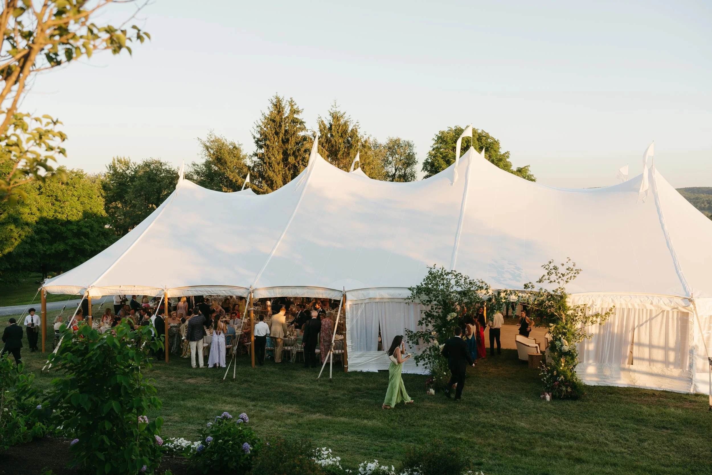 Greenery-wrapped tent entrance with surrounding garden florals at golden hour