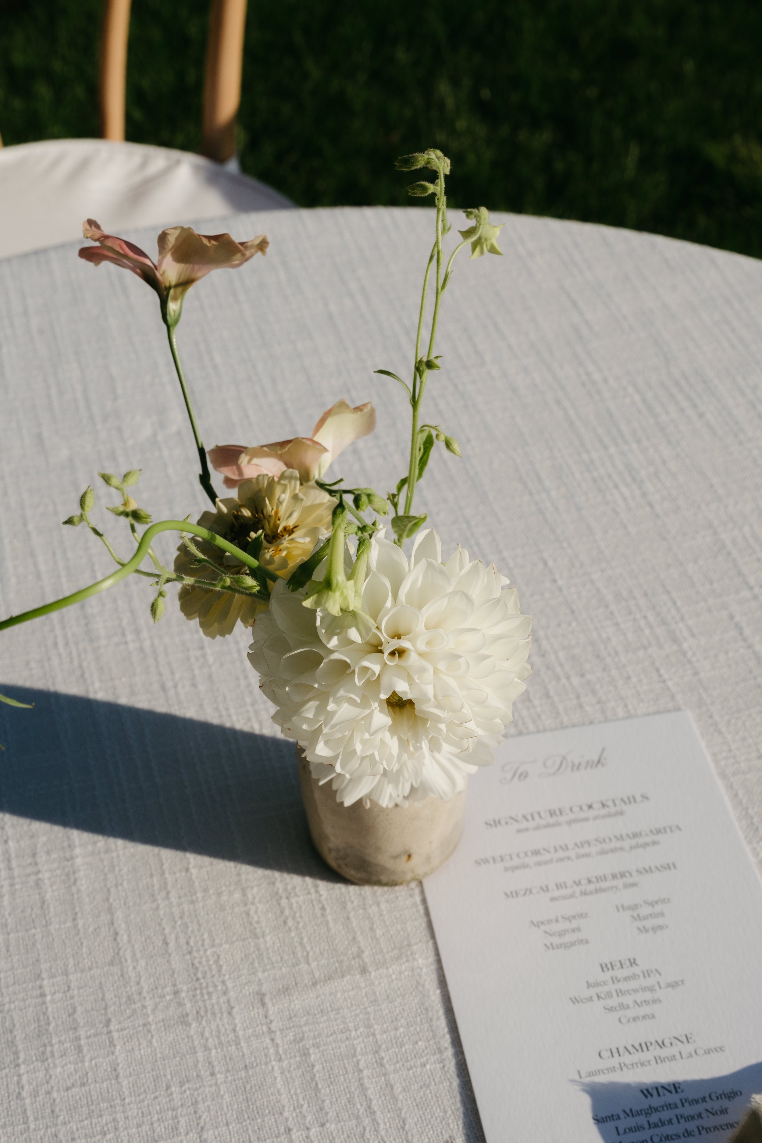 White dahlia arranged in small ceramic bud vase on linen-covered table