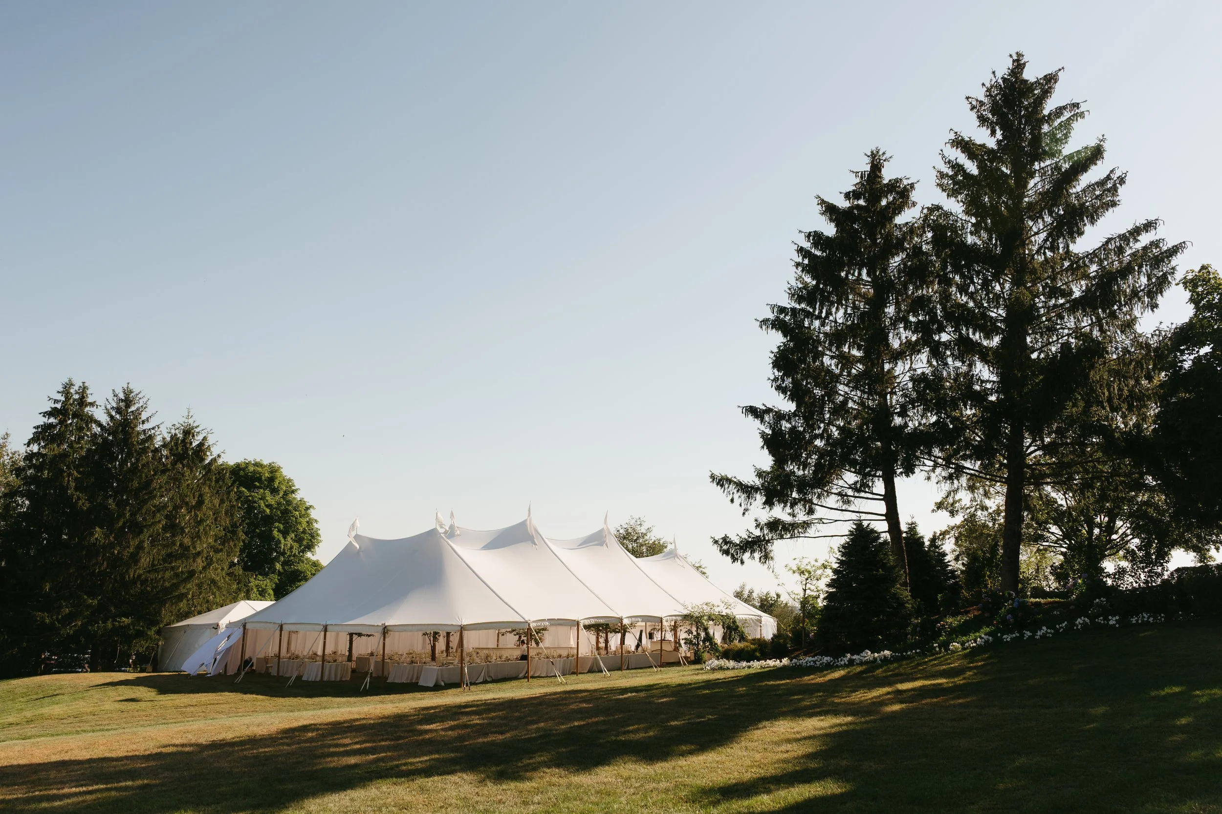 Reception tent framed by floral-lined aisle and hillside landscape