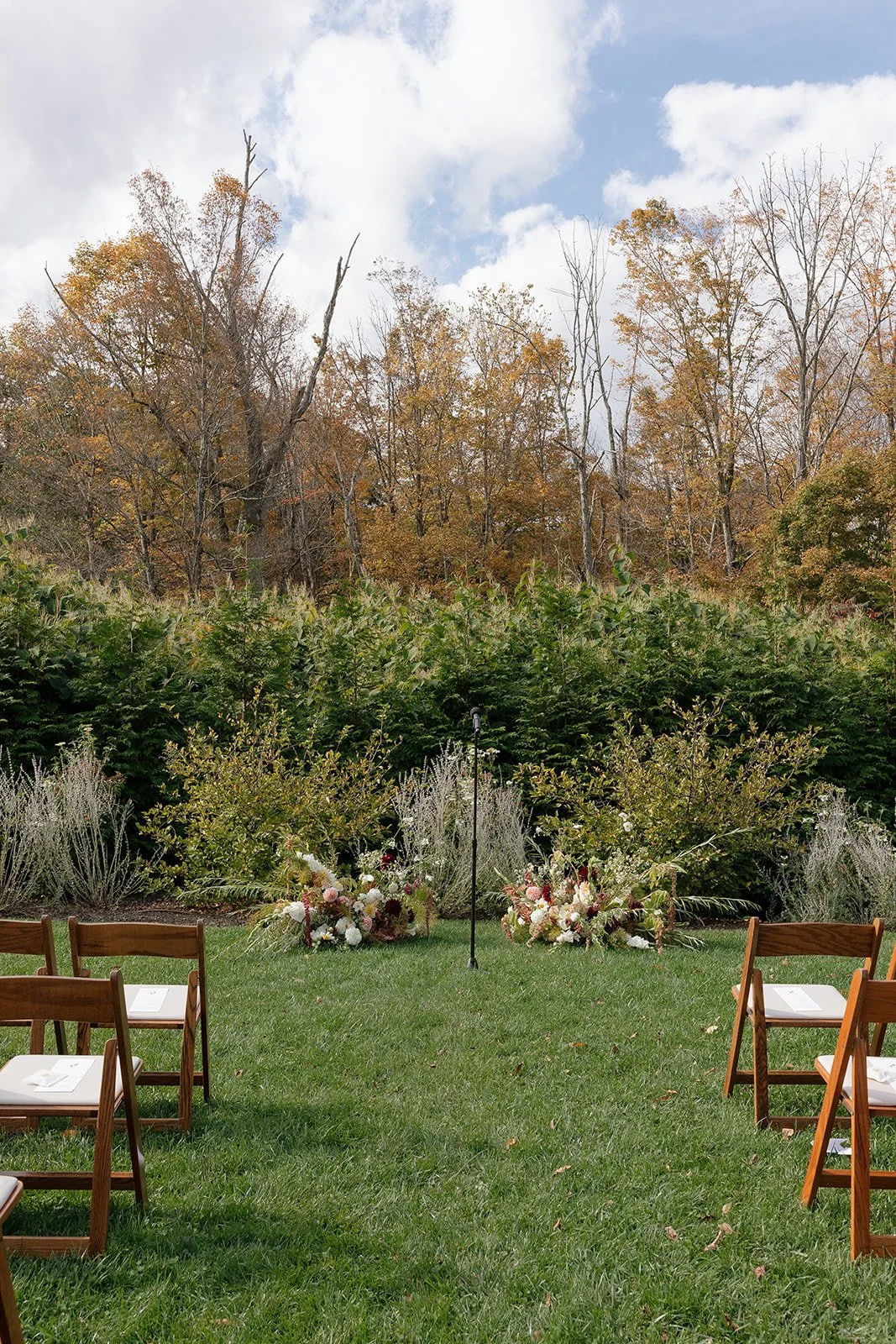 Outdoor ceremony aisle framed by meadow-inspired floral arrangements in early fall tones.