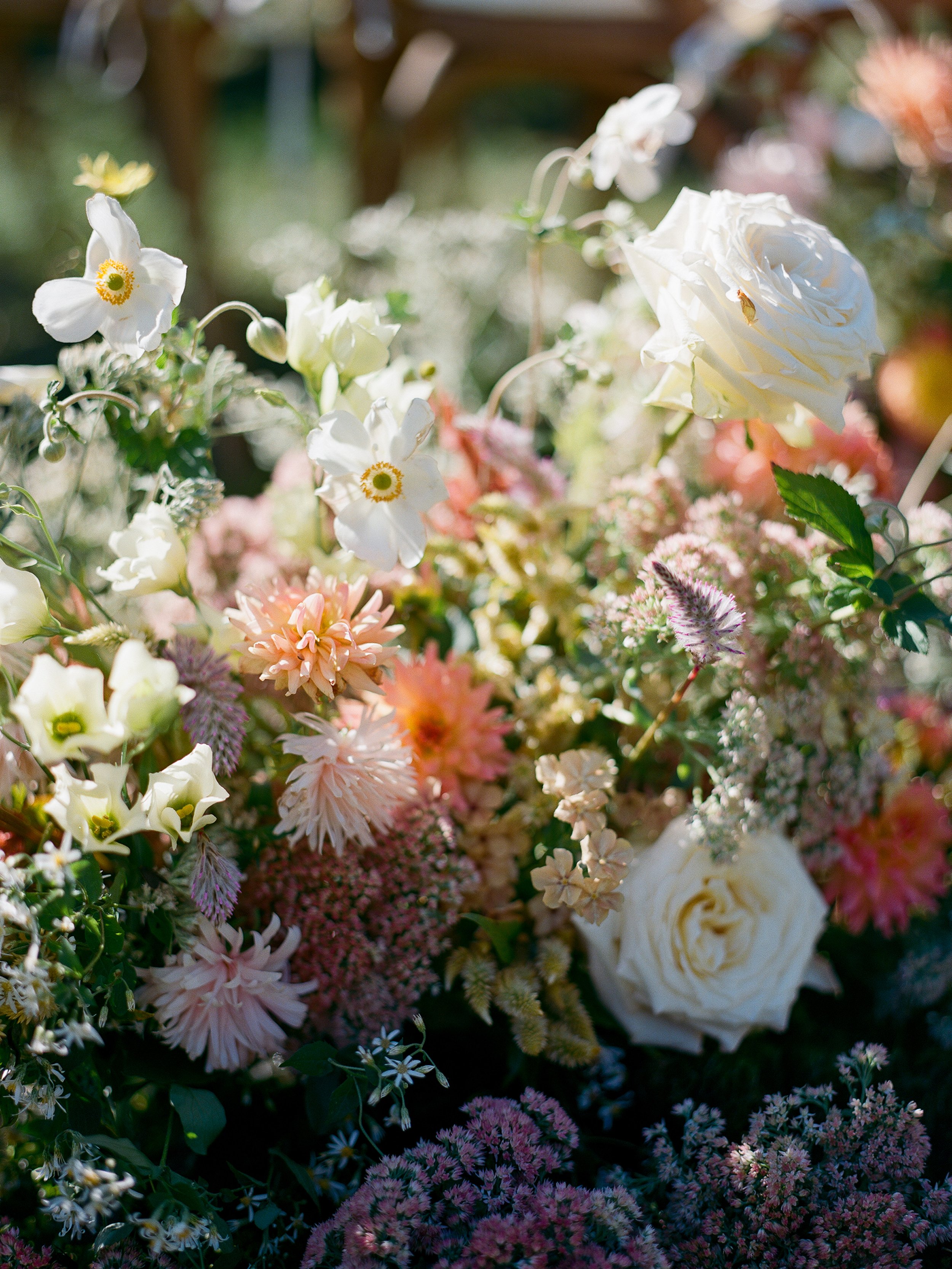 Ground floral arrangements lining ceremony aisle beside wooden chairs