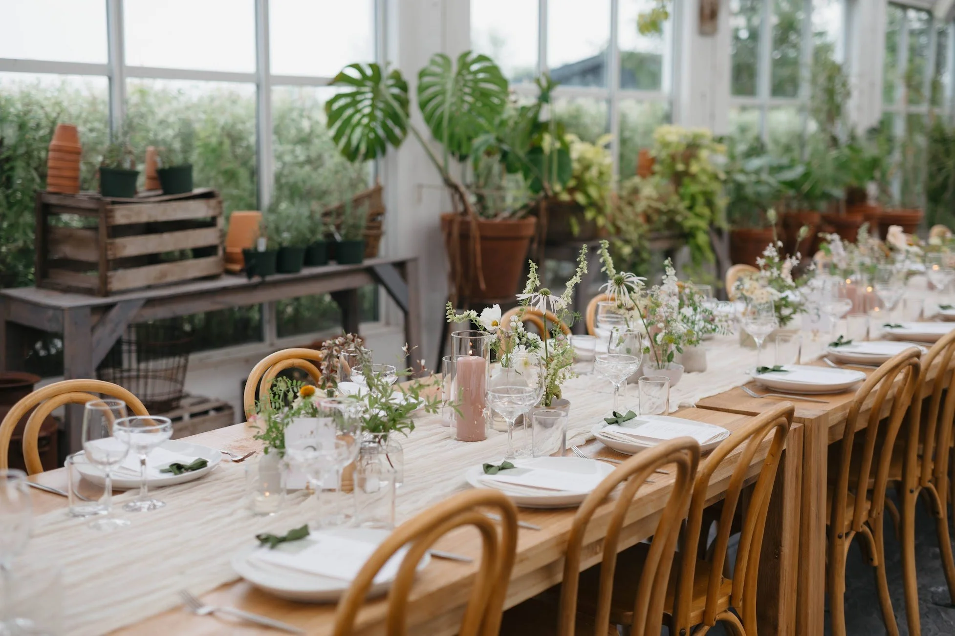 Long wooden wedding reception table with cute, delicate florals decorating the center alongside large candles.
