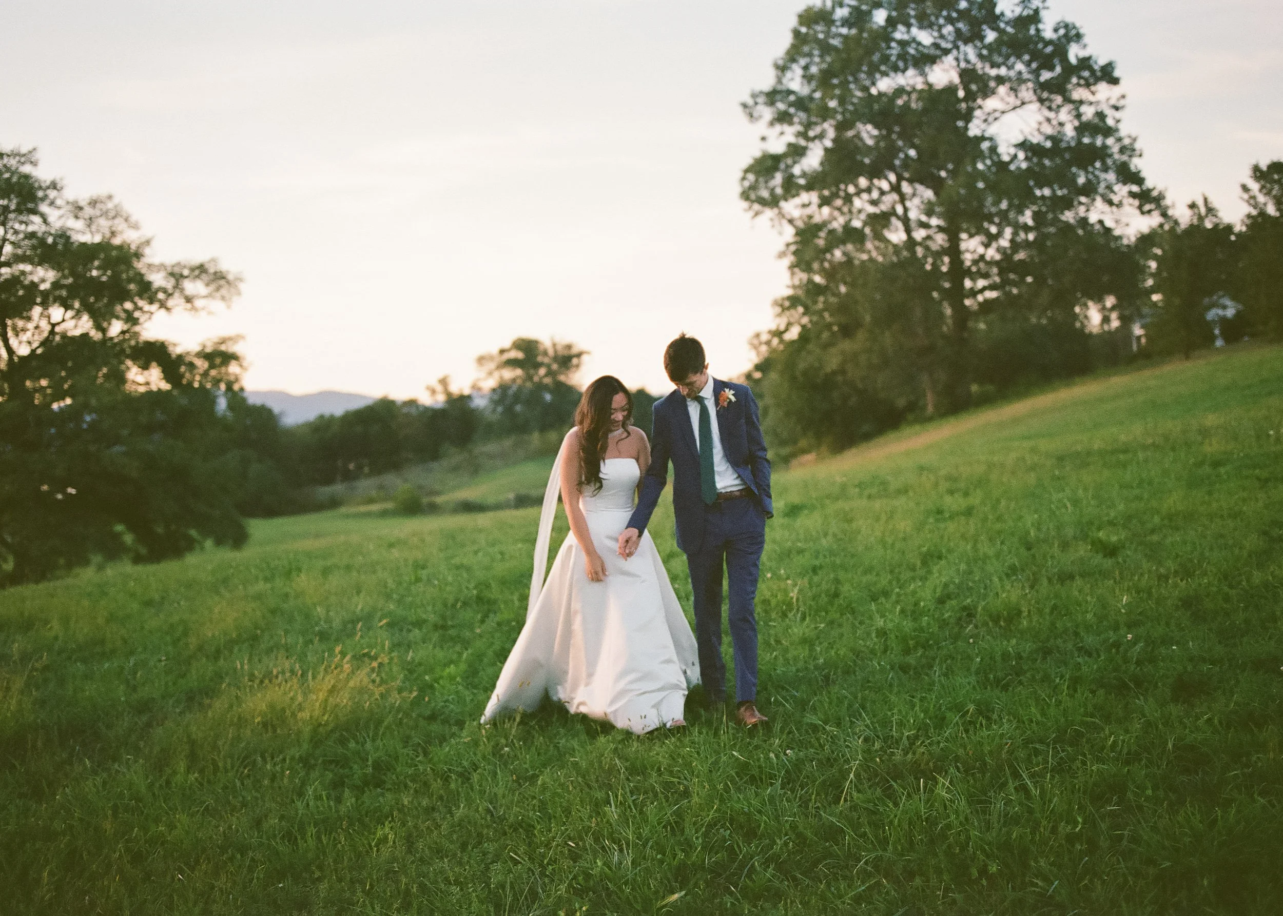Bride and groom walking together across an open field at sunset