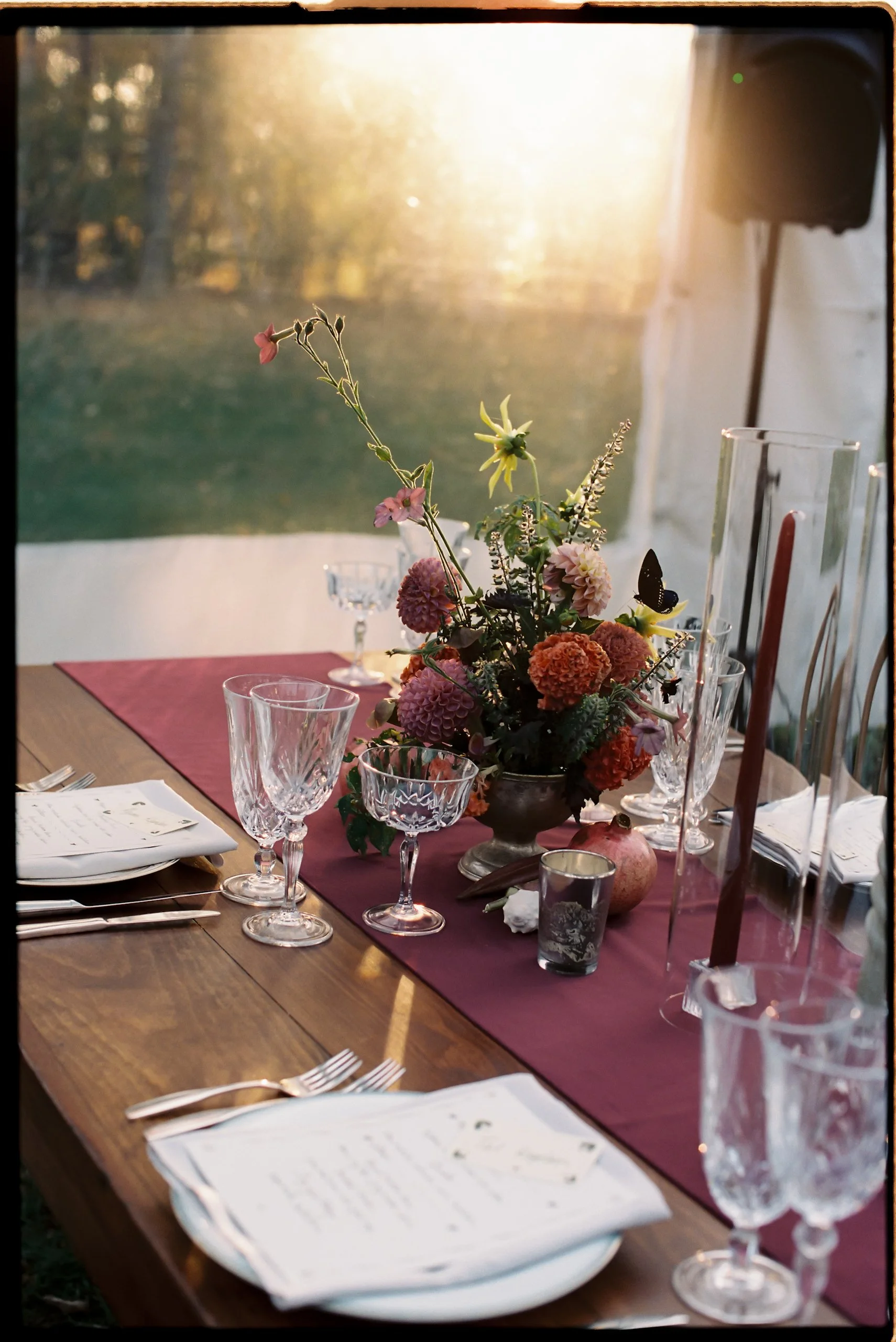 Intimate tablescape with sculptural floral arrangement catching warm sunset light inside the tent