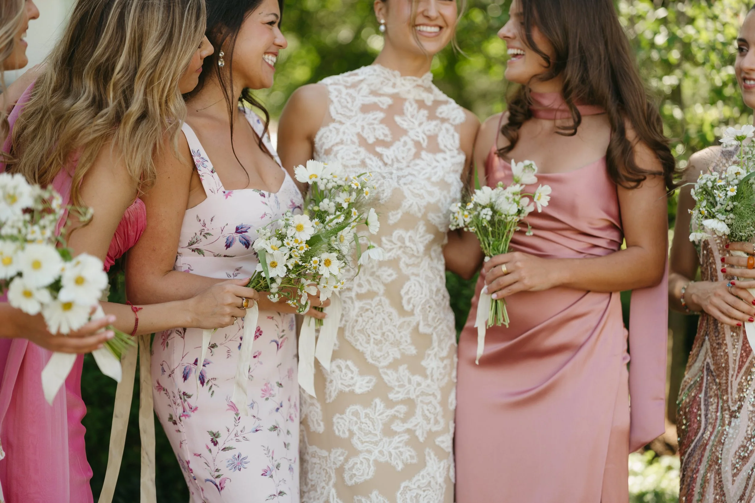 Bride laughing with bridesmaids holding simple white floral bouquets