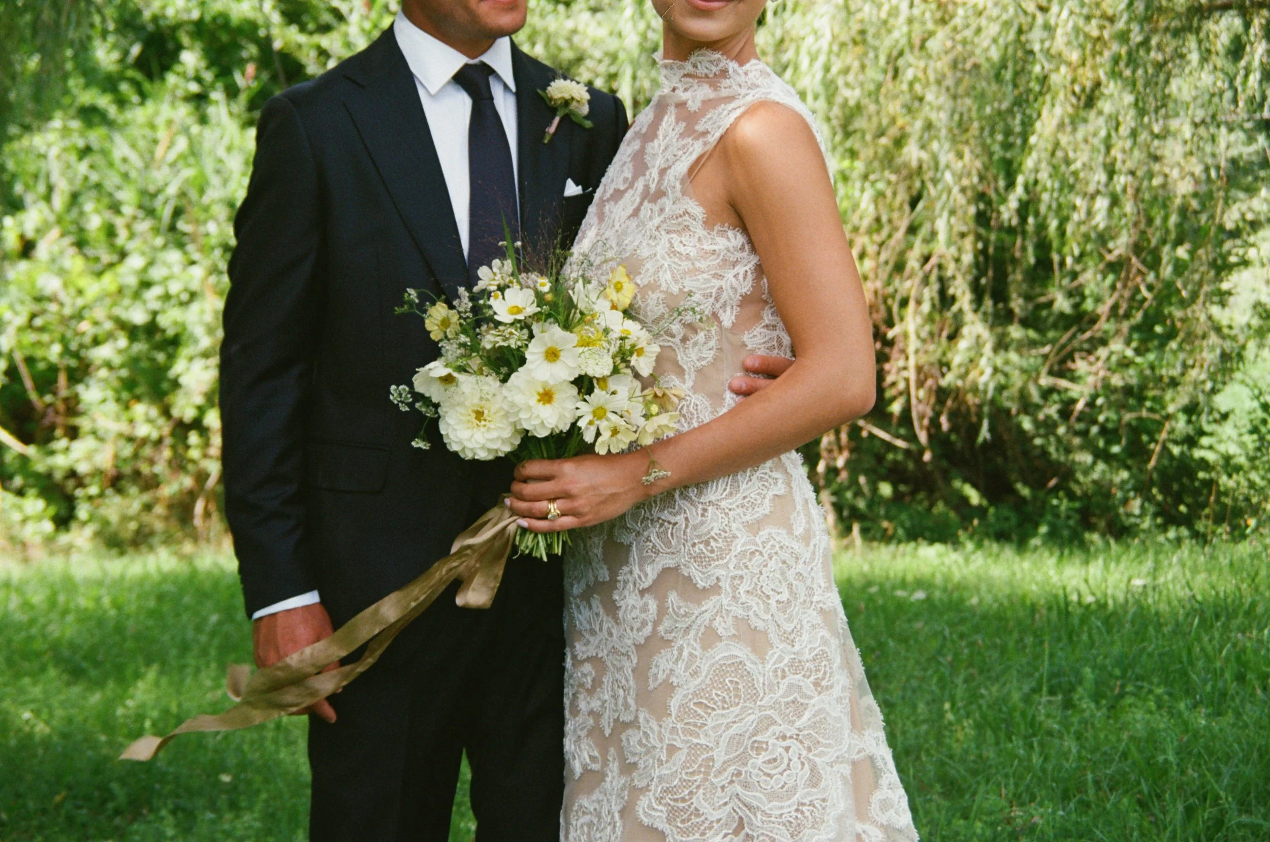Bride and groom standing together outdoors holding white garden-inspired bouquet
