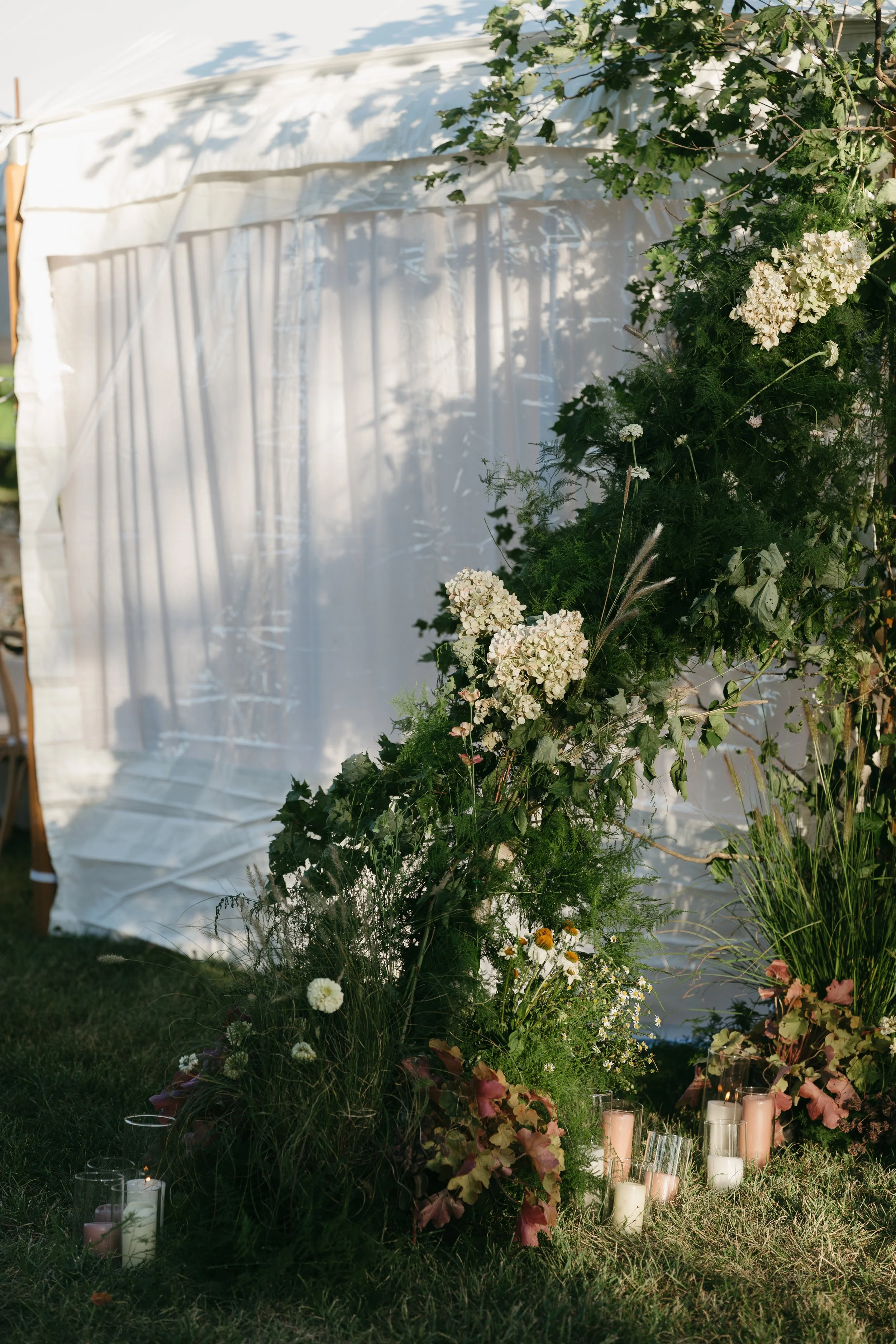Close-up of tent entrance featuring seasonal blooms, greenery and pillar candles