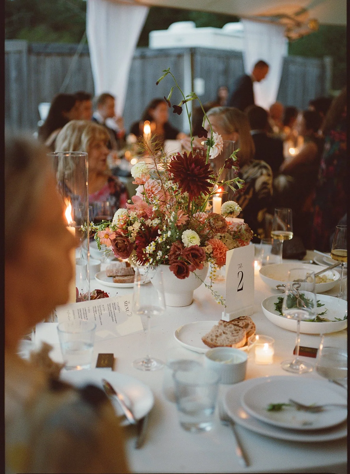 Candlelit reception table featuring warm-toned floral centerpiece with garden roses and late-season blooms