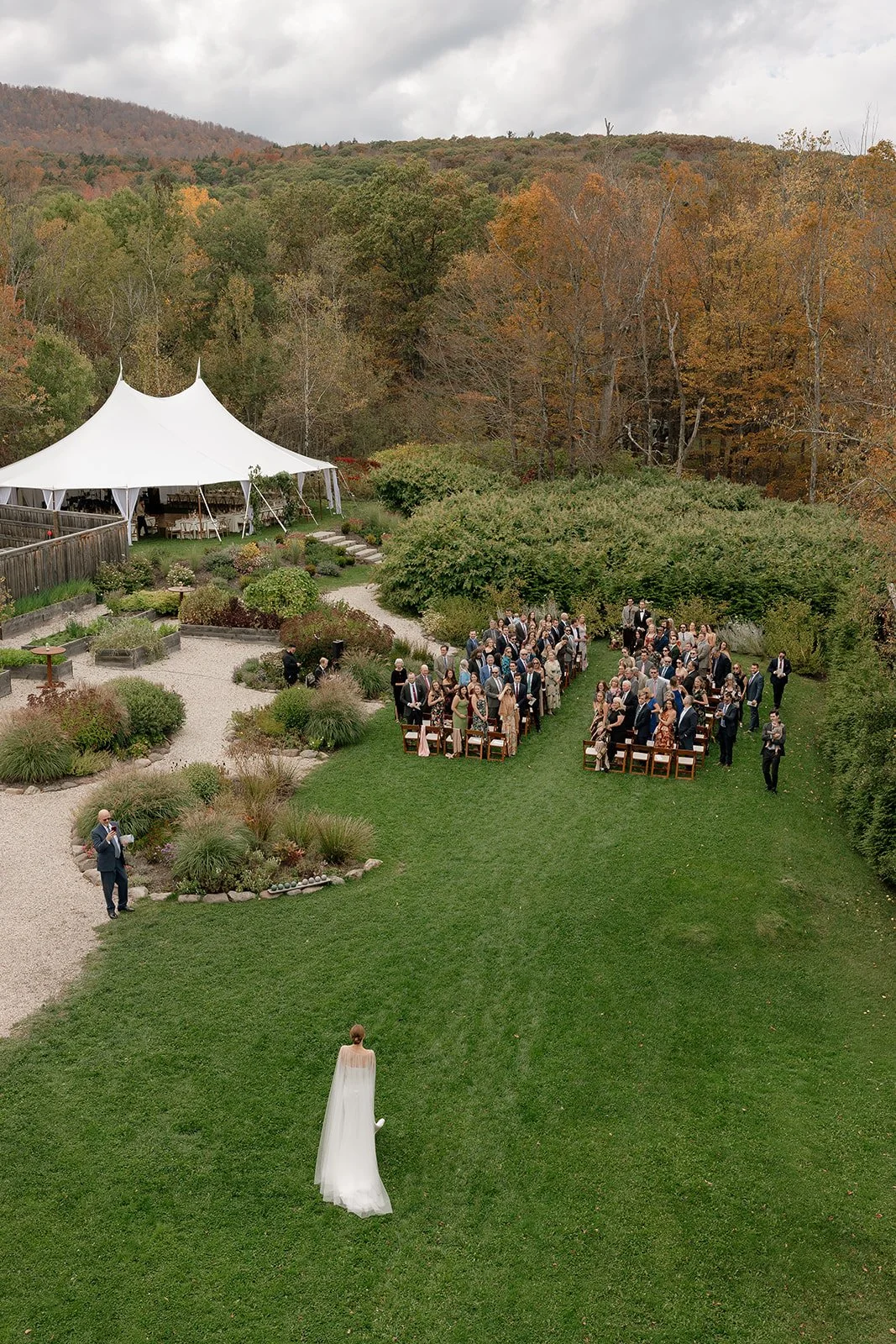 Aerial view of an outdoor ceremony set in lush gardens, with meadow-style floral arrangements framing the aisle.