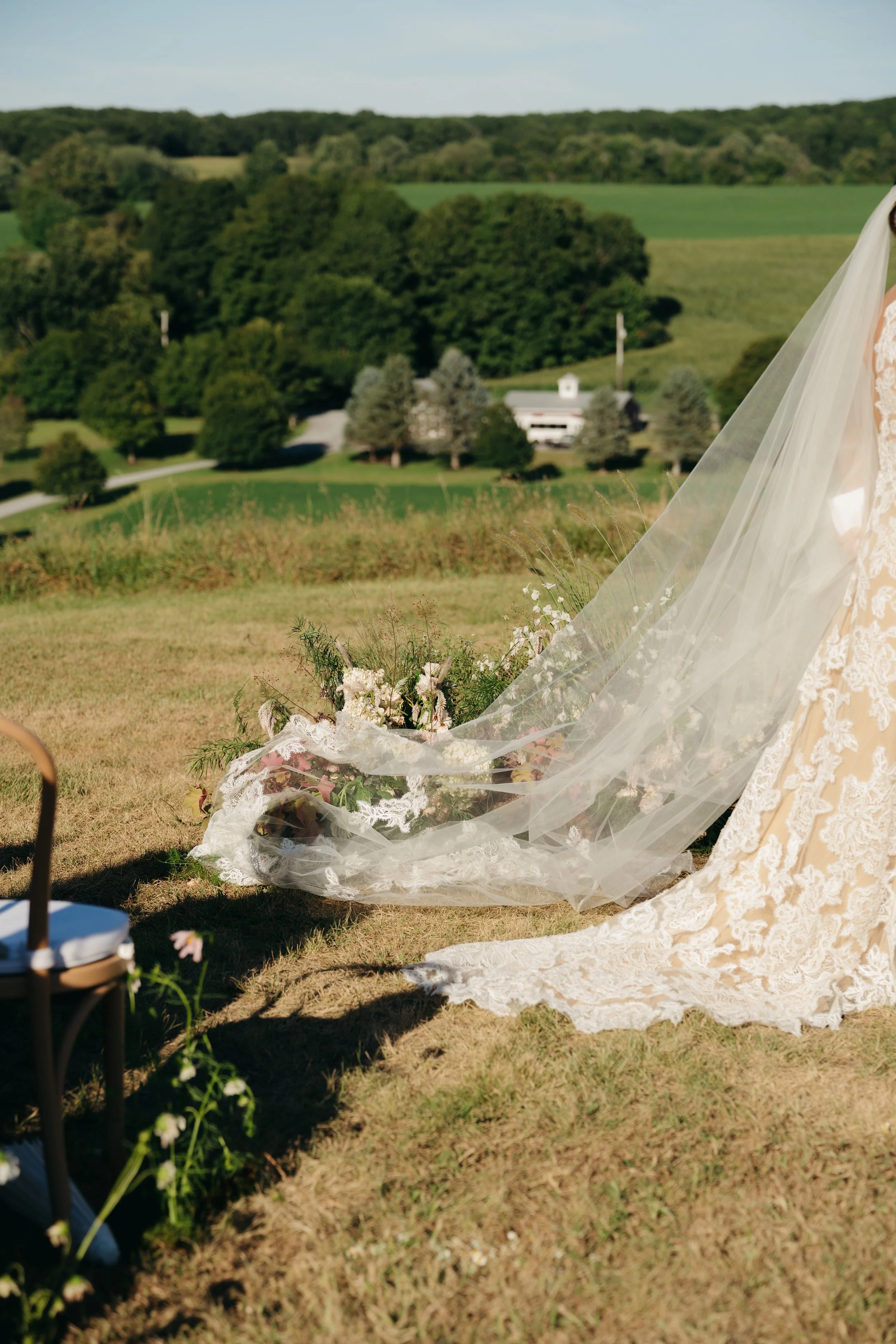 Ceremony florals and trailing bridal veil set against rolling countryside
