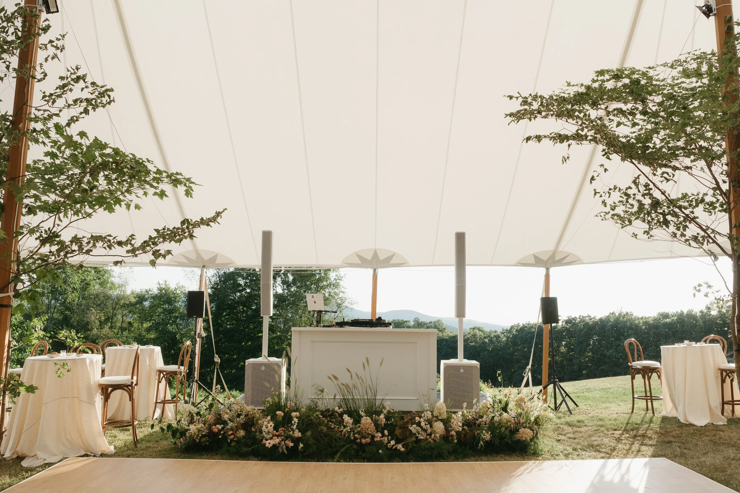 Low meadow-style floral arrangements framing reception stage beneath tent