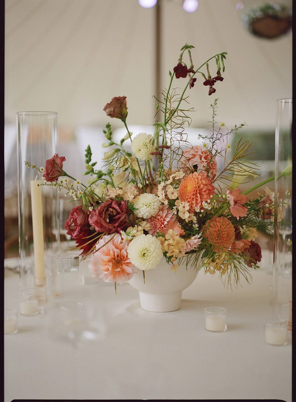 Lush autumn wedding centerpiece with dahlias, lisianthus, and seasonal foliage in a soft ceramic vessel