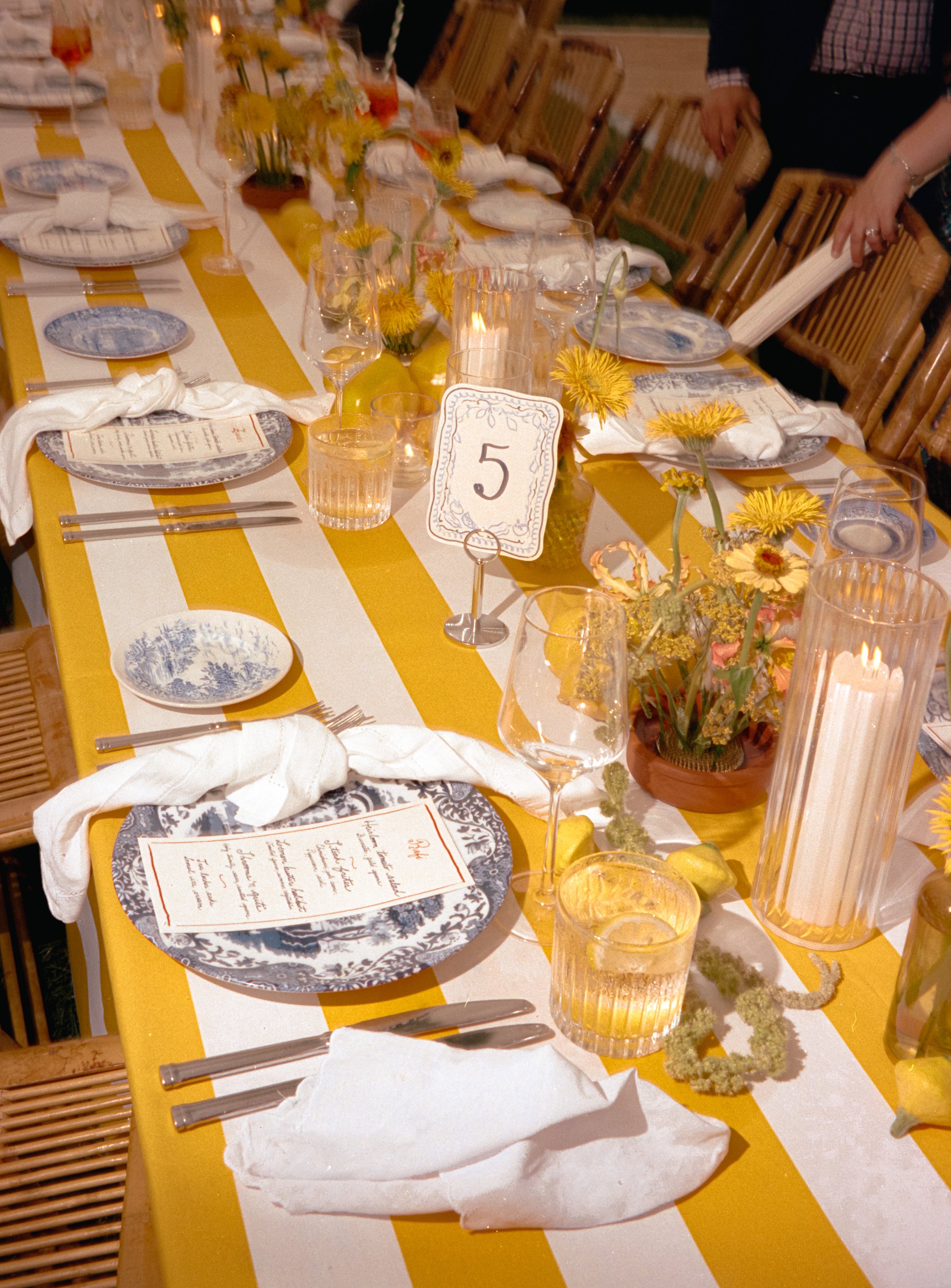 Close-up of striped reception table with yellow linens, floral centerpiece, menus, and candles