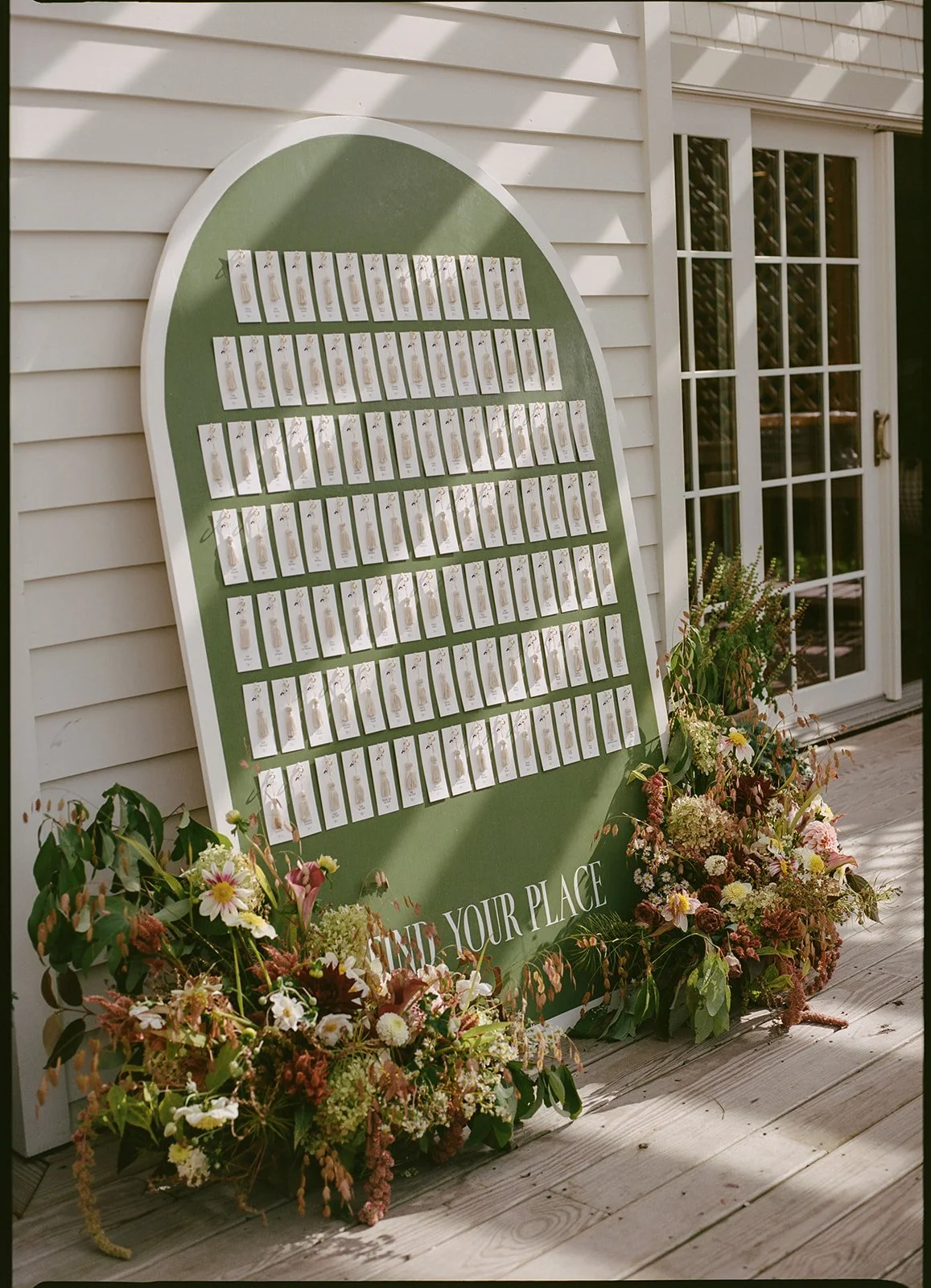 Curved escort display framed by abundant seasonal florals with textured greenery and warm fall color.