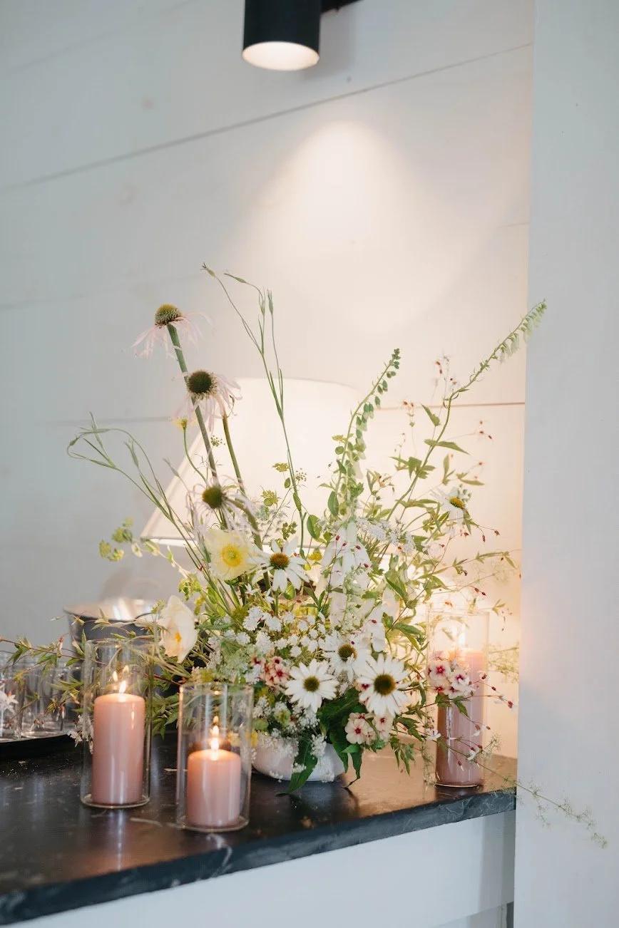 romantic, lush bouquet with signature, fresh flowers next to pink pillar candles in glass on marble countertop