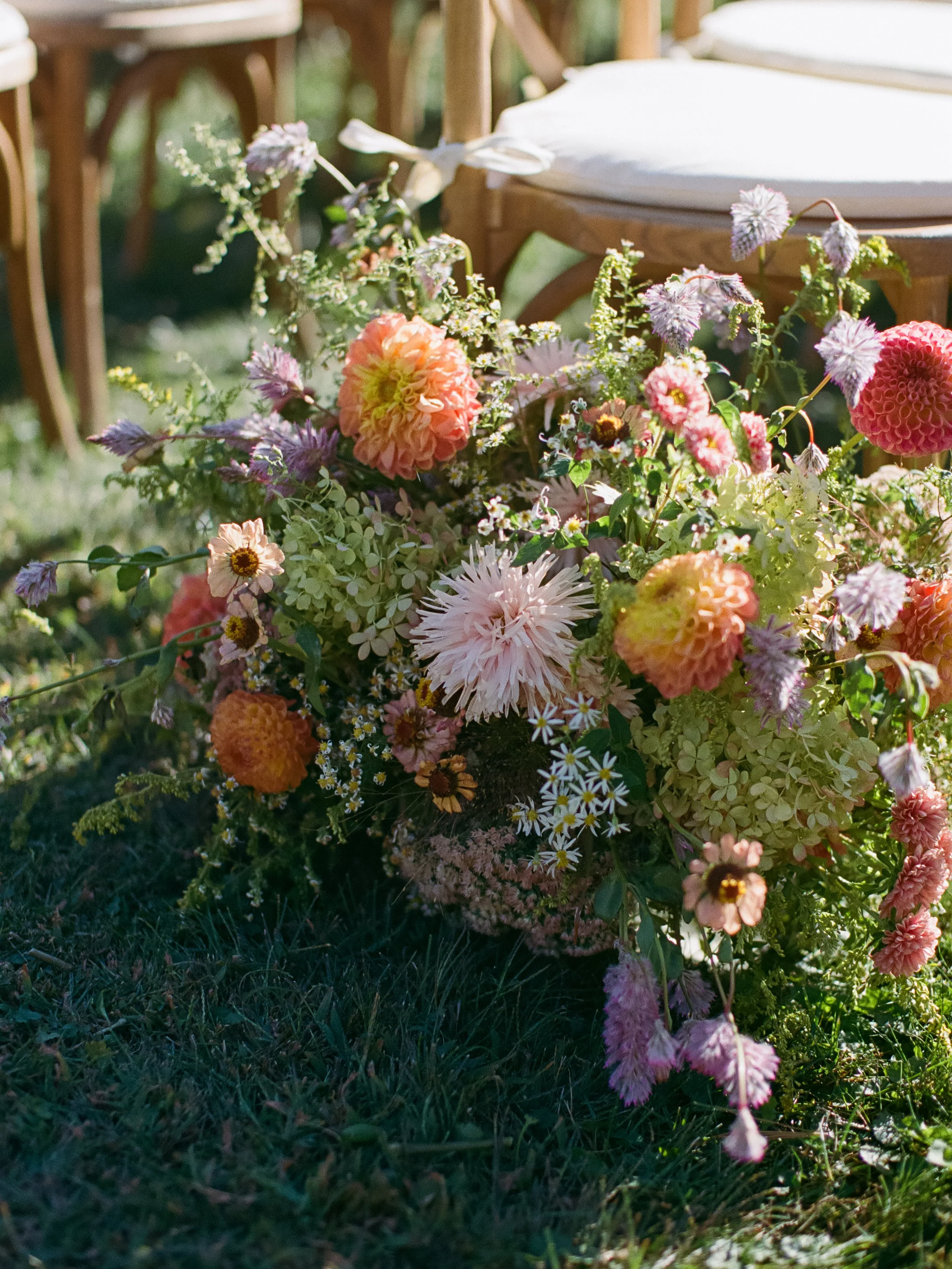 Garden-style ceremony flowers arranged at the base of wooden chairs