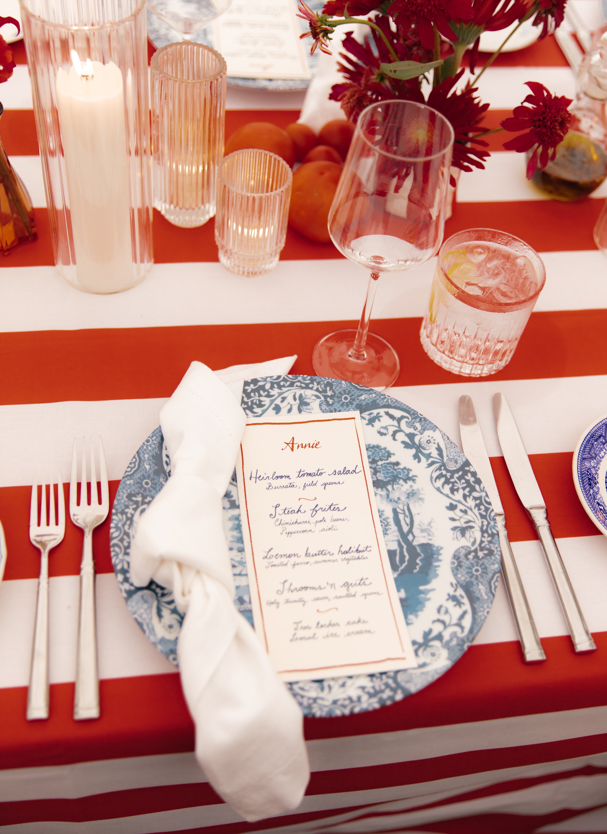 Place setting with striped red-and-white linens, patterned plate, menu card, and candle