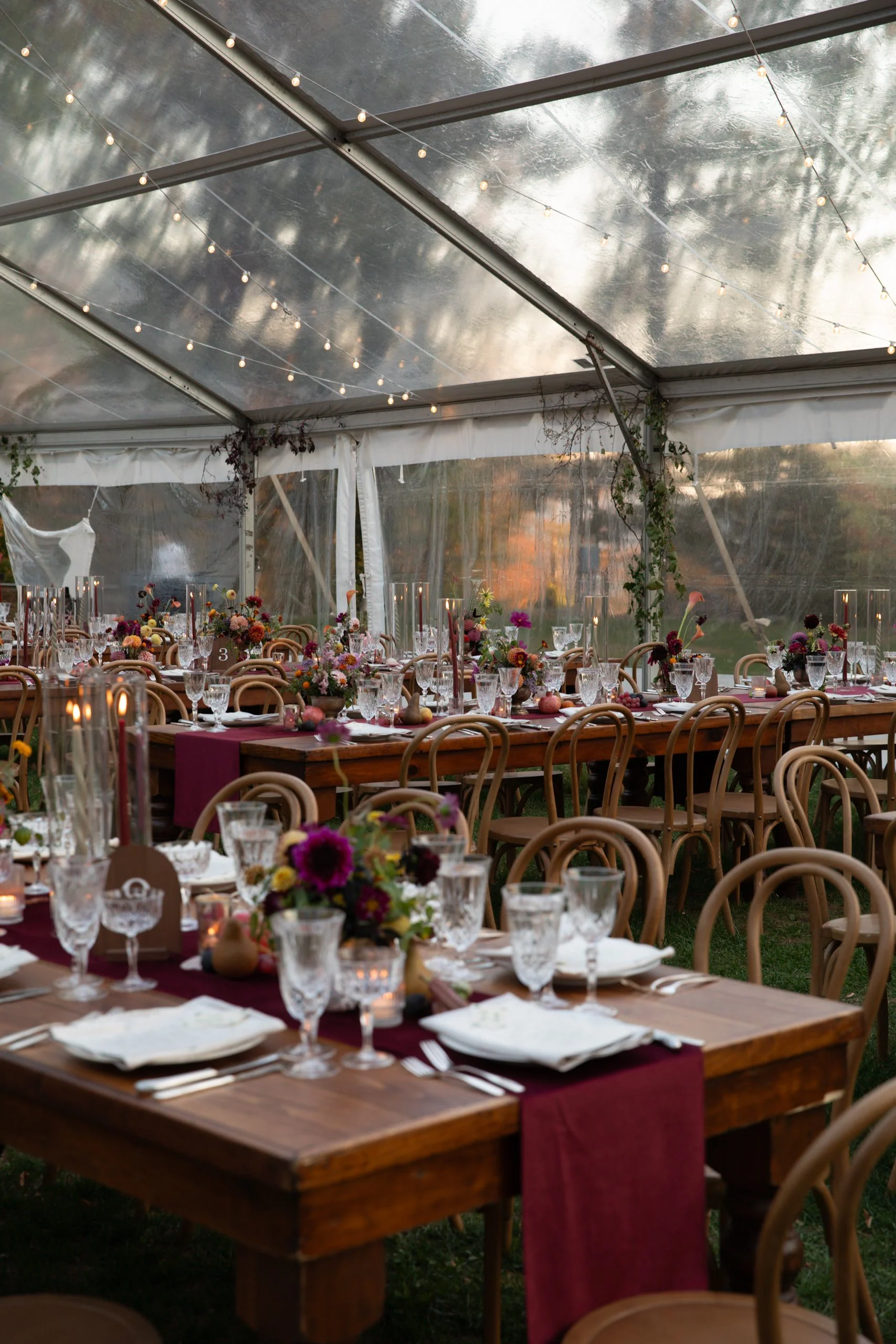 Long reception tables beneath a clear tent, styled with abundant fall floral centerpieces in deep berry, rust, and gold tones