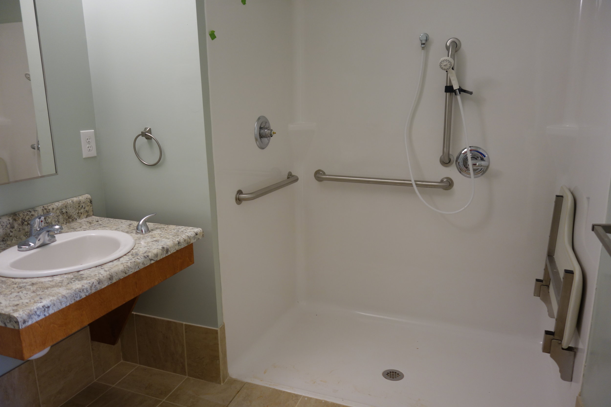 An accessible bathroom with handrails and a fold down seat for accessibility