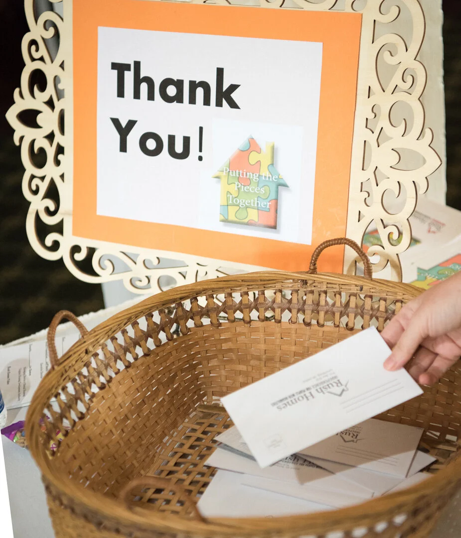 A hand is dropping a donation envelope into a basket in a thank you sign next to it.