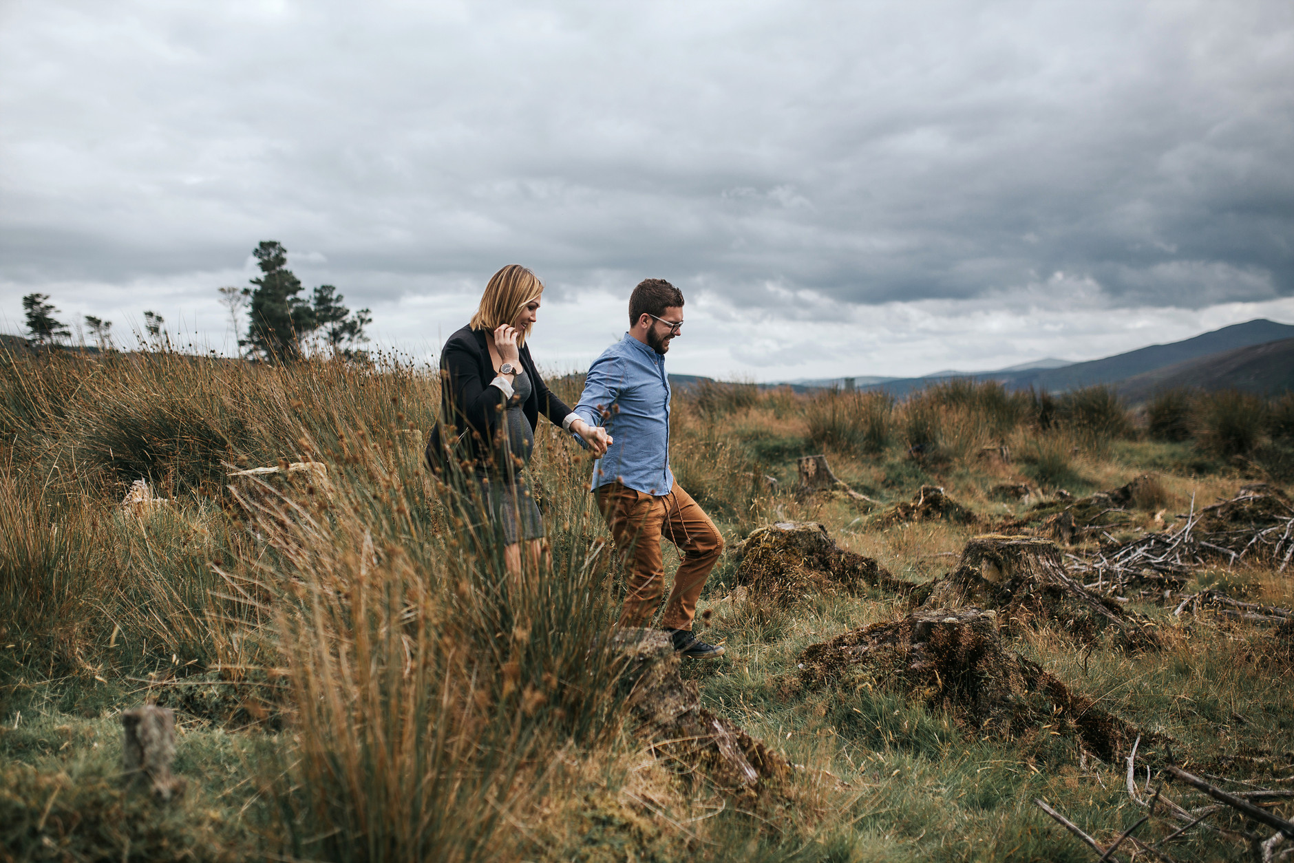 Couple holding hands and laughing while walking in the grass in Dublin mountains