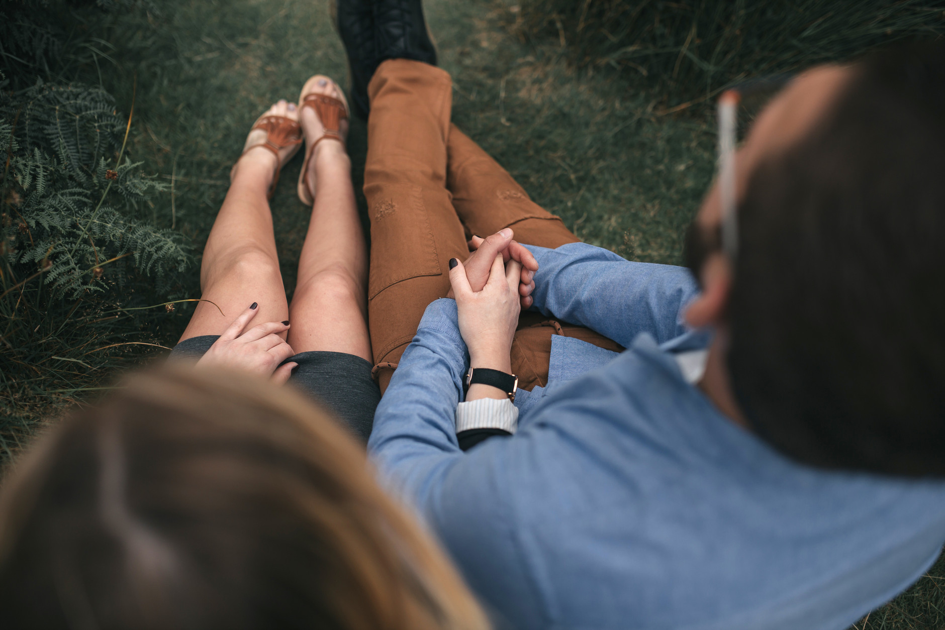 Couple sitting in the grass and holding hands while looking in the same direction
