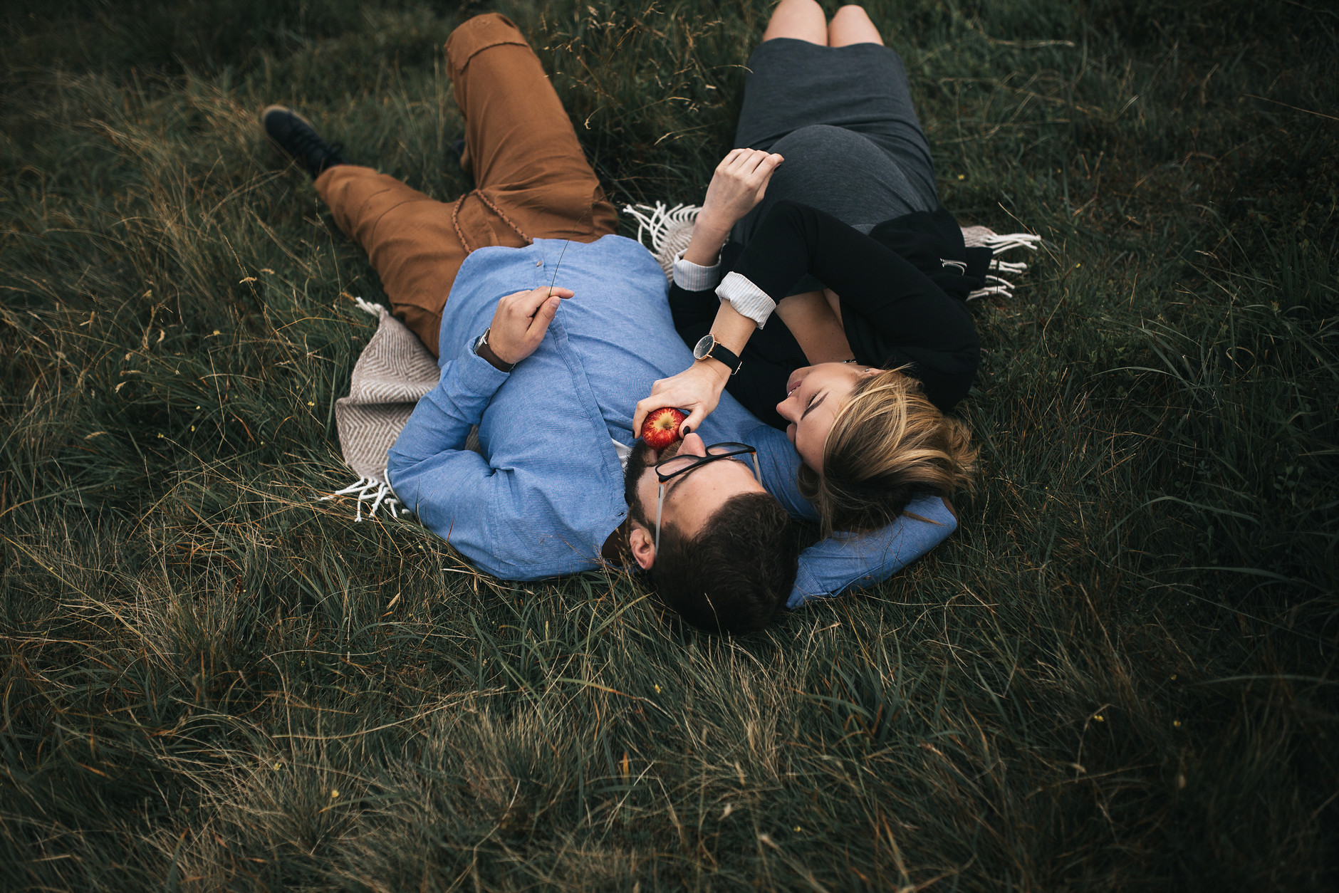Pregnant woman giving an apple to her husband while they lie on the ground