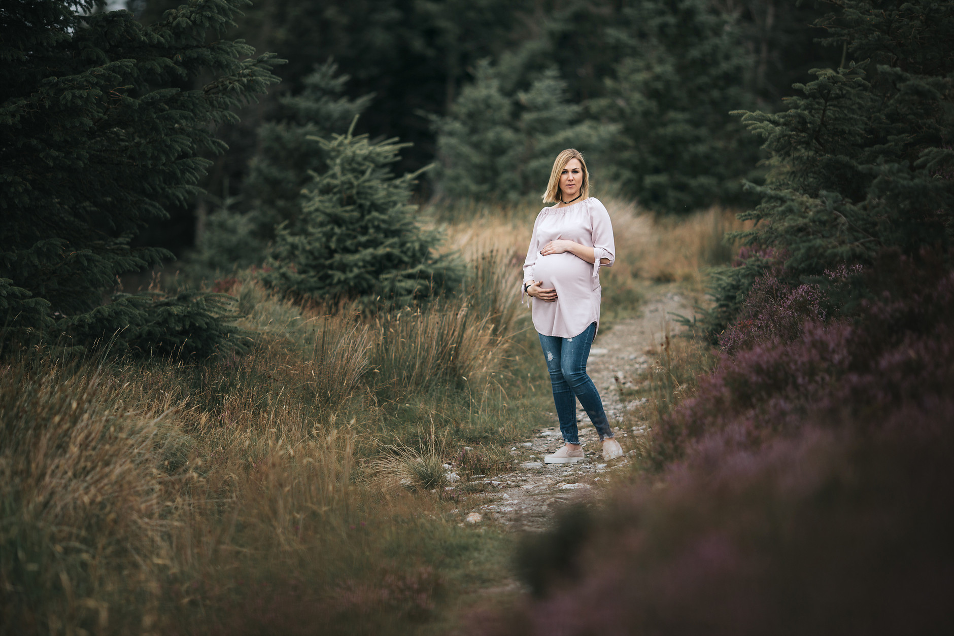 Portrait of a pregnant mother in a pale pink blouse and jeans looking at the camera