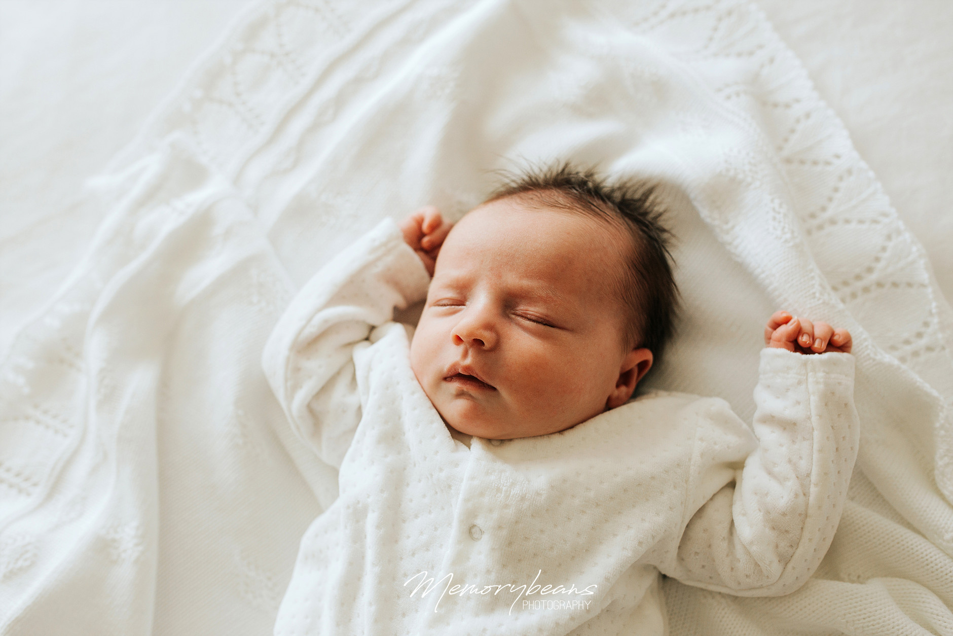 Sleeping newborn baby with dark head of hair on white blanket