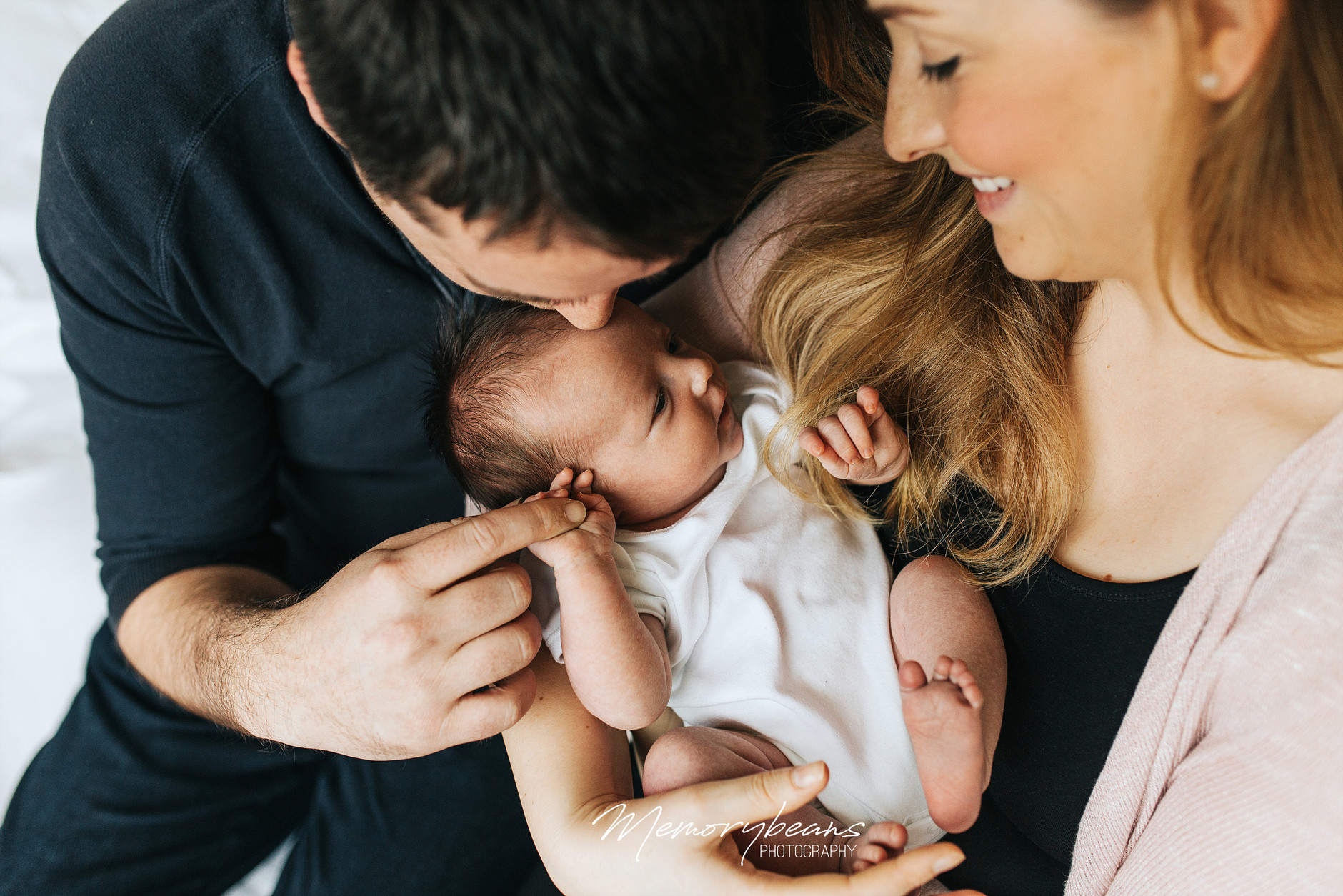 Family photo of newborn baby with his parents, holding father’s finger in his hand