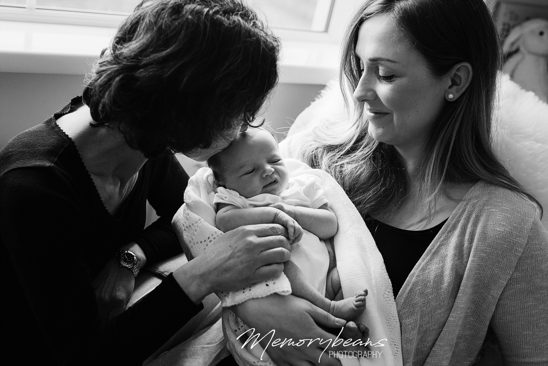 Grandmother kissing newborn baby on his head while his mother holds him