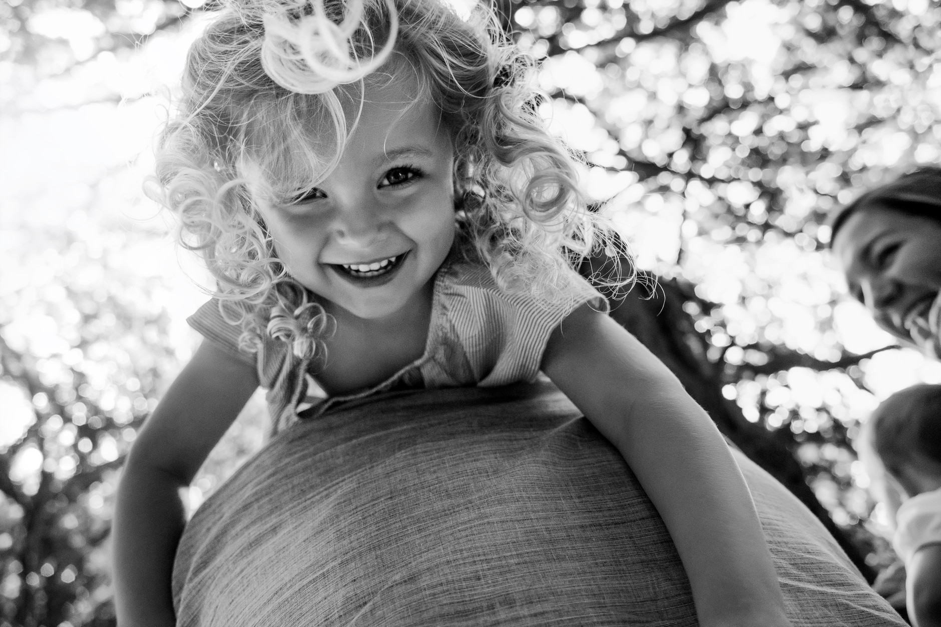 Little girl with blond curly hair laughing and hanging upside down on her father’s shoulder