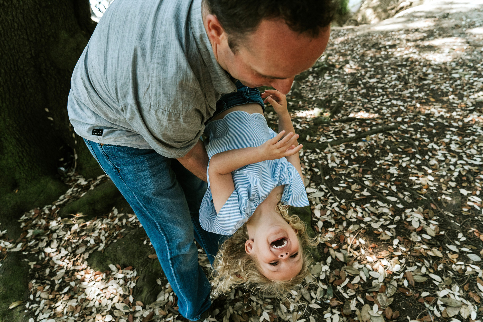 Little girl laughing while her dad swings her upside down: fun