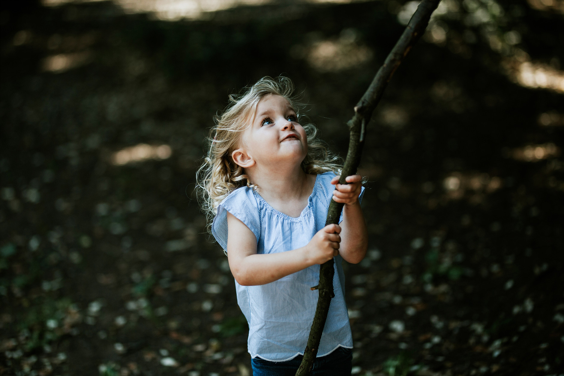 Little blond curly girl playing with a big stick in the park on their vacation in Dublin