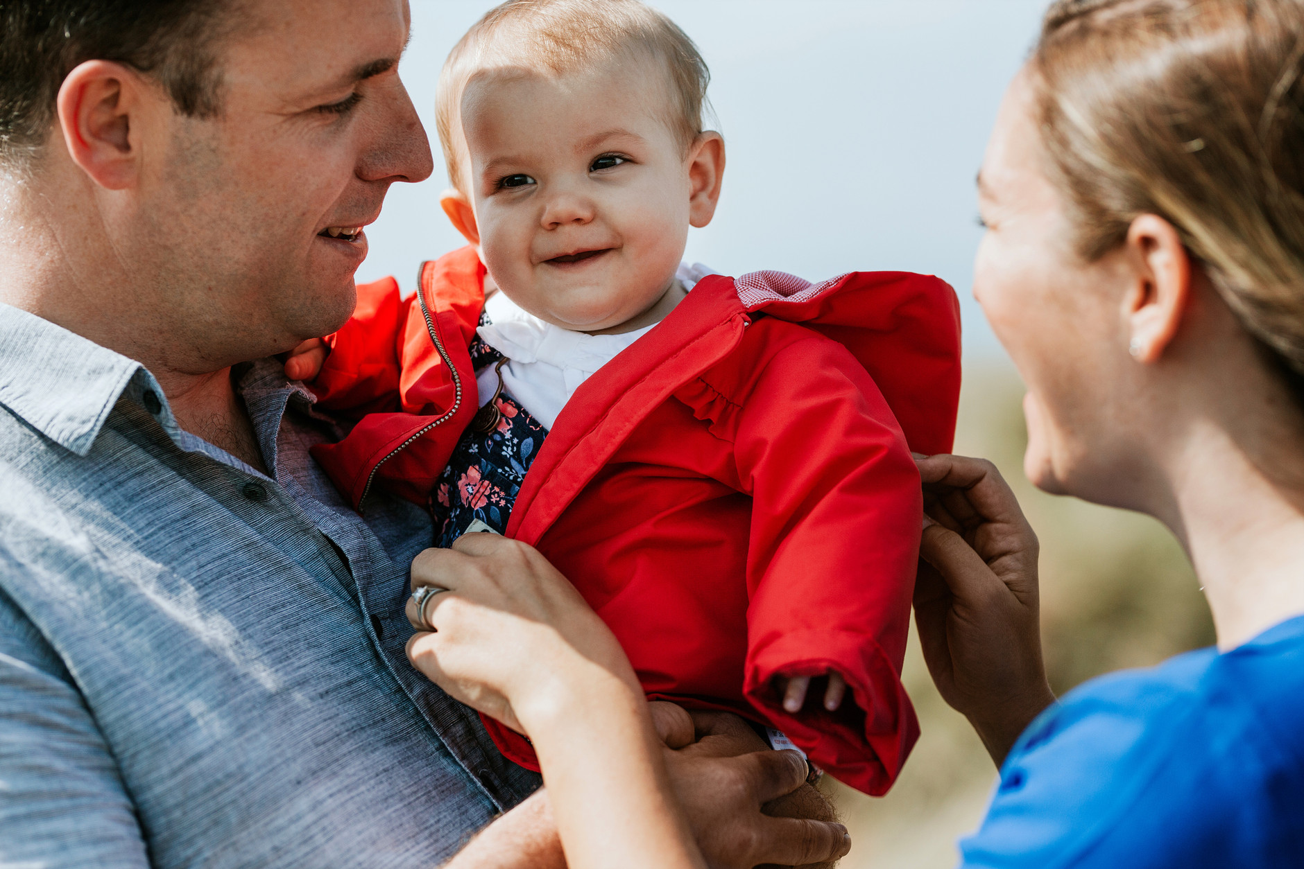 Little baby girl in red coat in her father’s arms and mother smiling