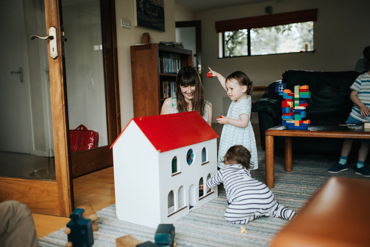 Big smile from a mother looking at her children playing with a toy house