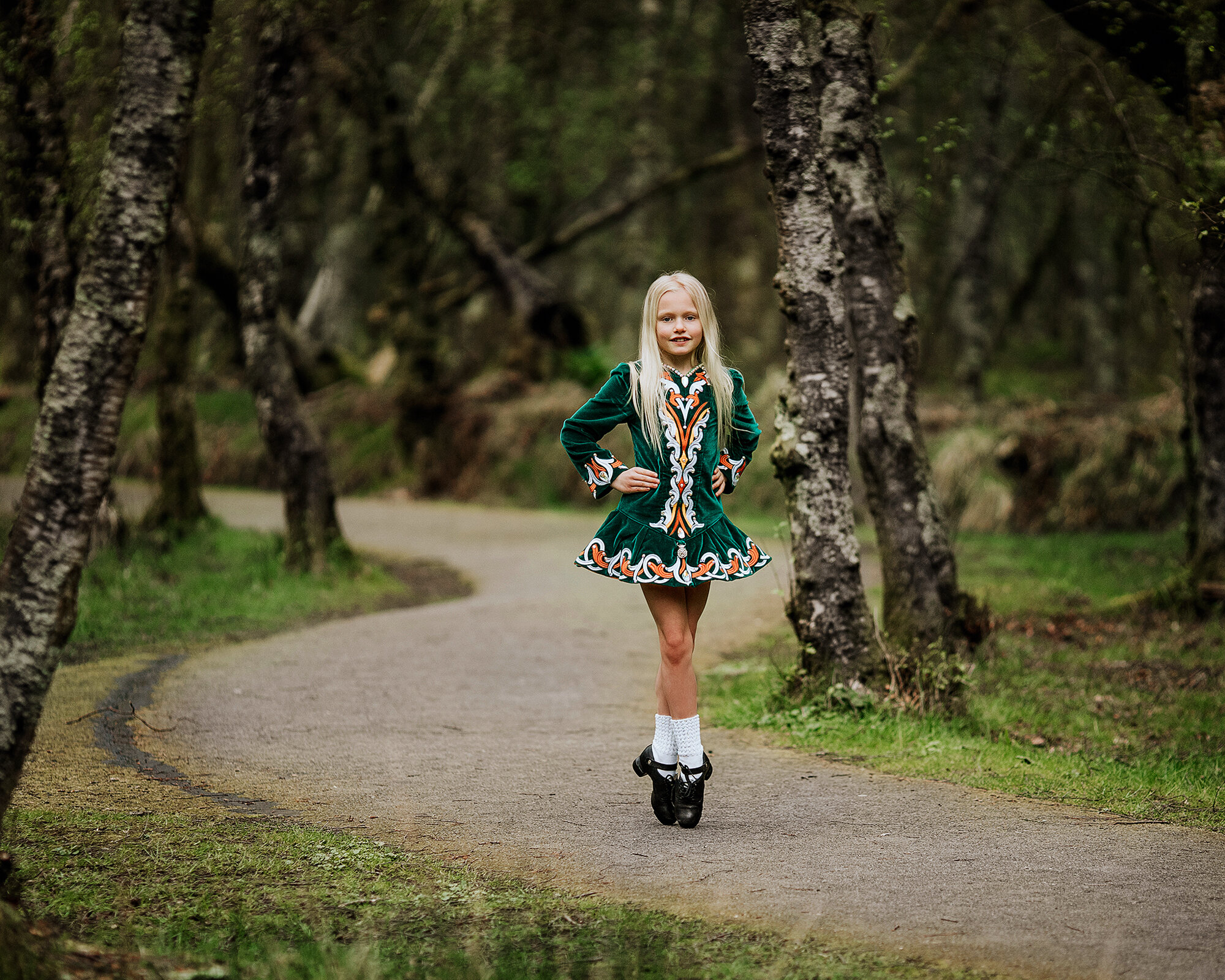 Irish dancer in her costume standing an point in the forest