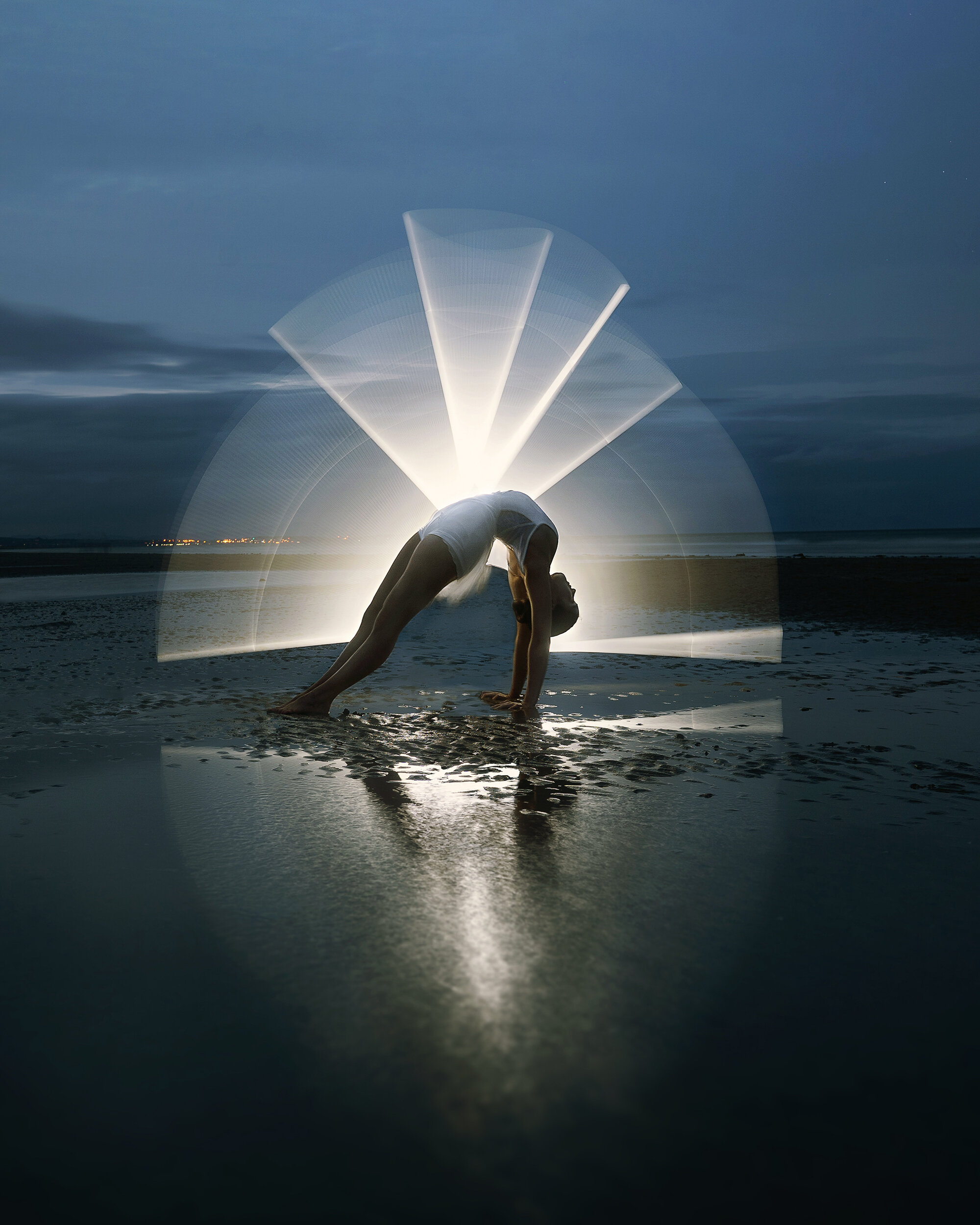 acrobatic dancer performing the bridge on the beach with light painting 