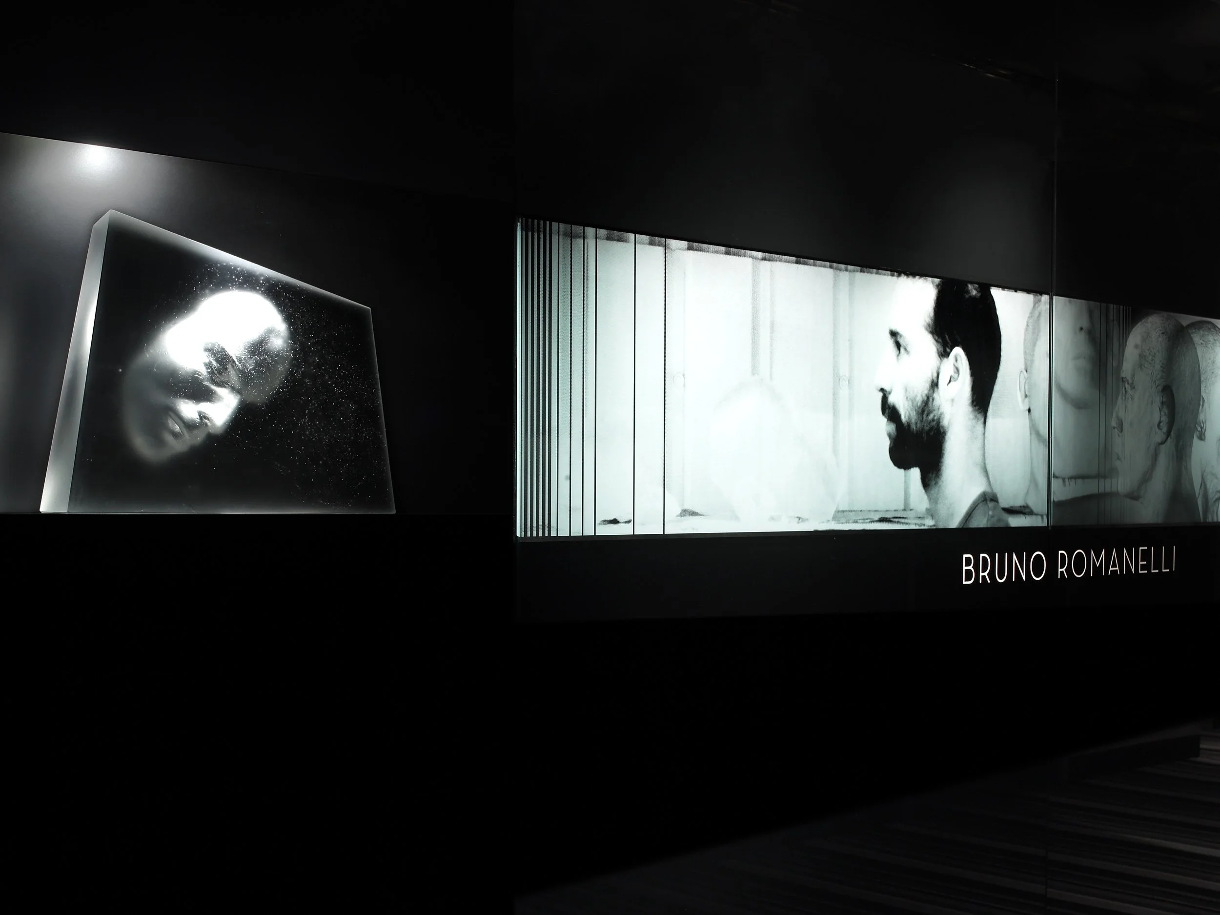 Black and white art display featuring a woman's face on a glass panel and a profile photo of a bearded man with the text "BRUNO ROMANELLI"