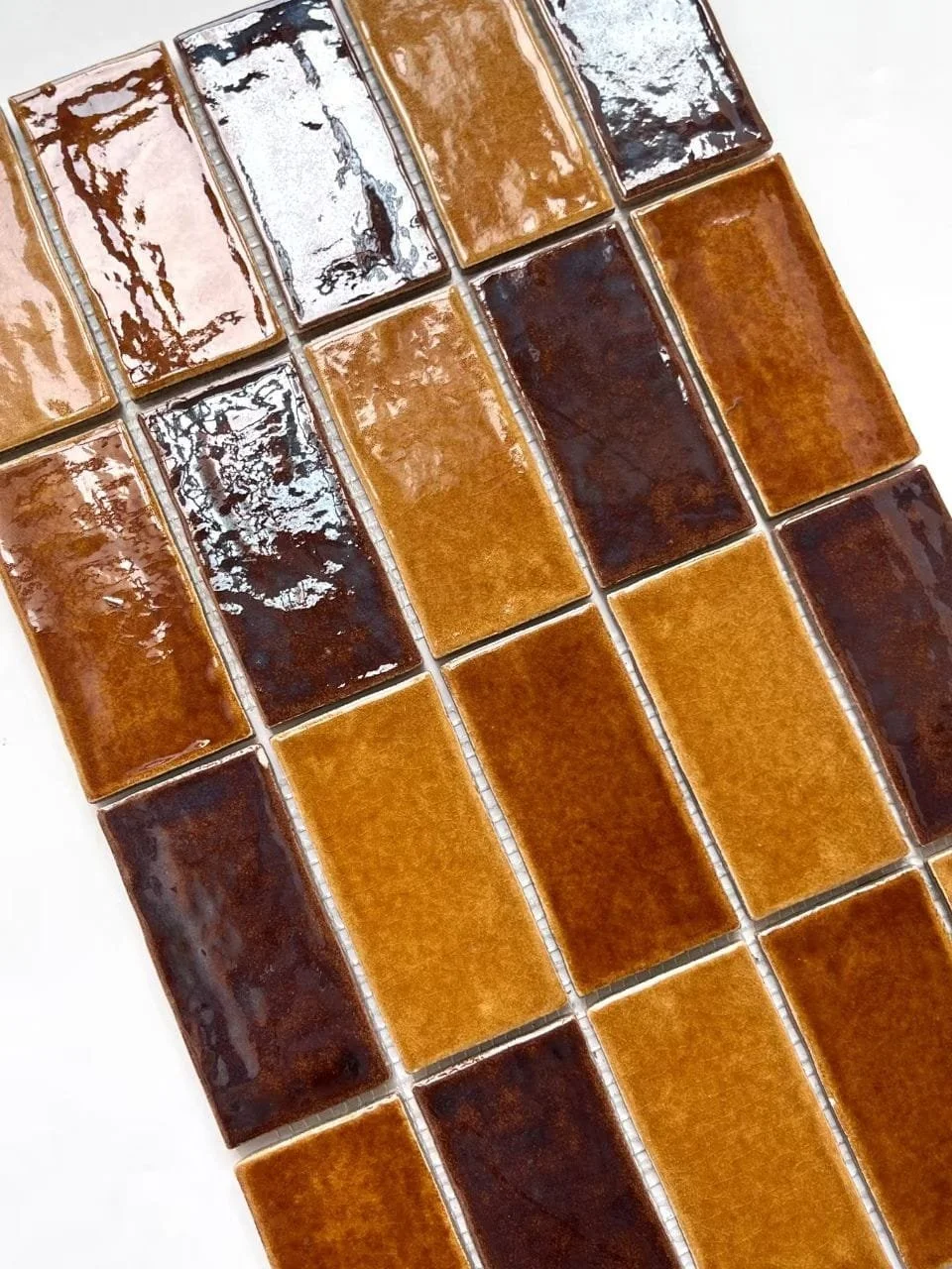 These glazed tiles feature a rich, multi-tonal palette of amber, rust, and deep brown, enhanced by a high-gloss finish that creates movement across the surface. The controlled variation in glaze pooling and tonal depth gives each tile a distinct look