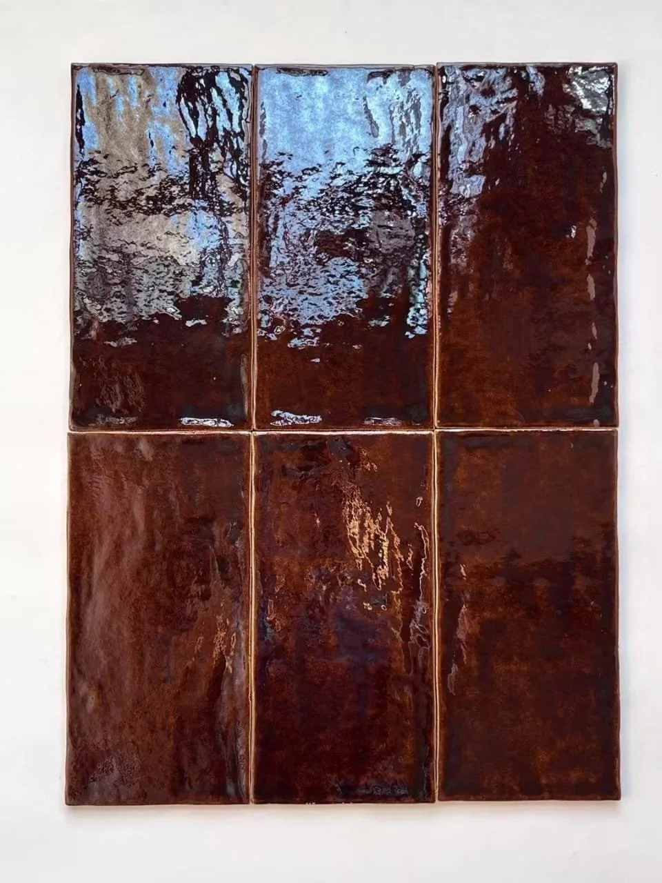 These glazed tiles feature a rich, multi-tonal palette of amber, rust, and deep brown, enhanced by a high-gloss finish that creates movement across the surface. The controlled variation in glaze pooling and tonal depth gives each tile a distinct look