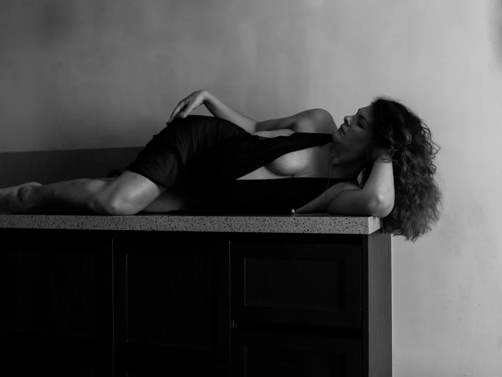 A woman in black lying along a kitchen counter, black and white.
