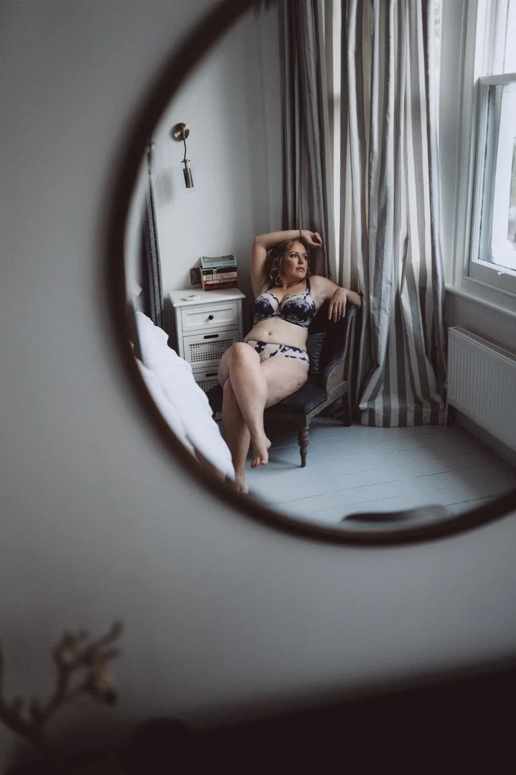 A woman reflected in a round mirror, sitting by the window.