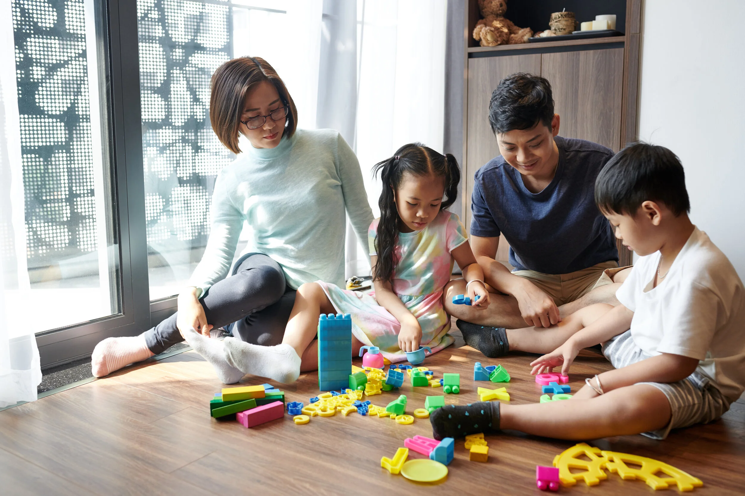 Model family of four playing on the floor with blocks.