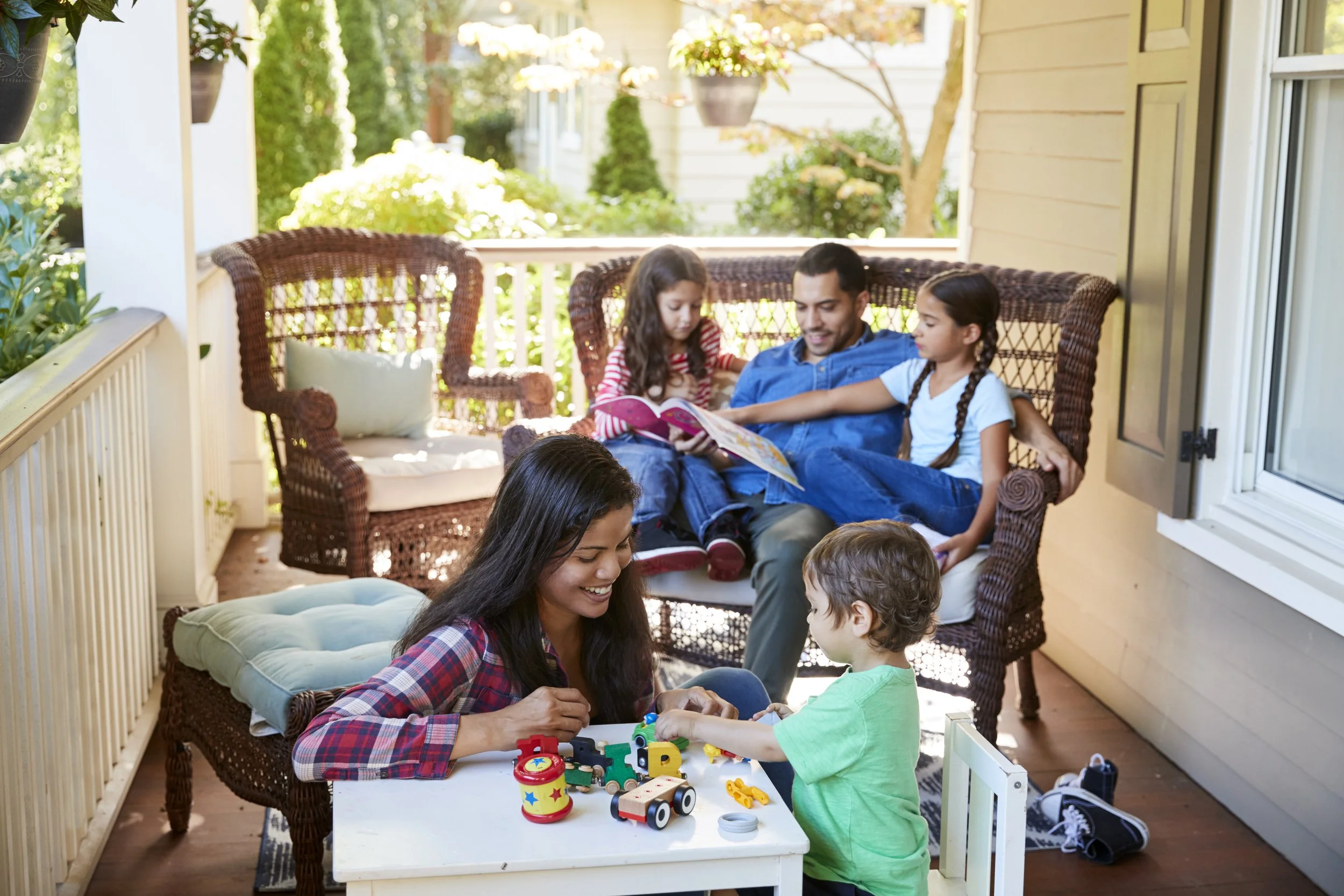 A model family of four sitting on a porch, reading a book together.