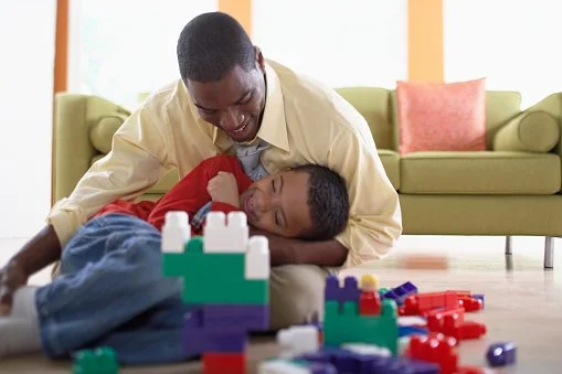 A model and a model child happily building with colorful Legos on the floor.
